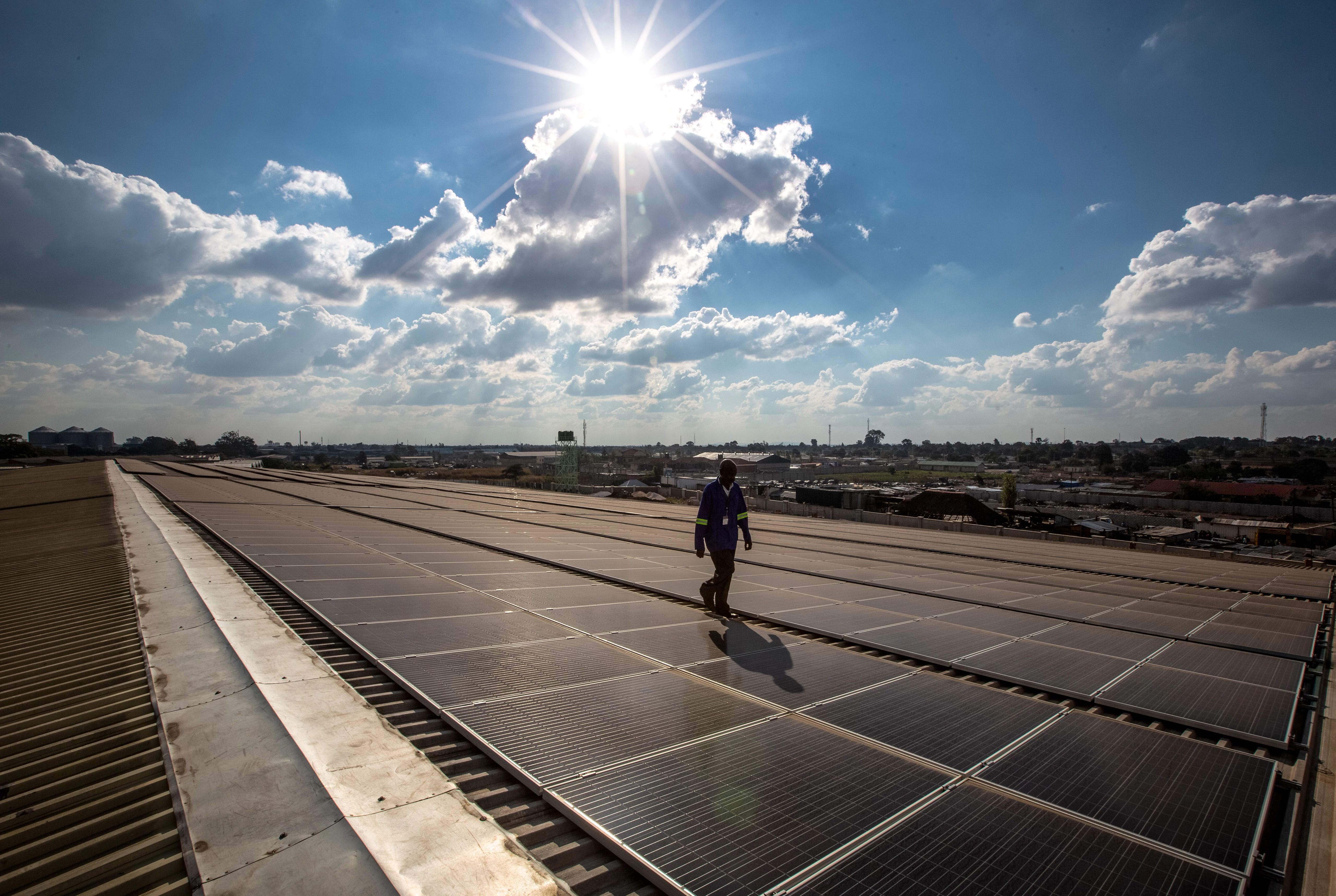 A technician walks among solar panels against a blue sky.