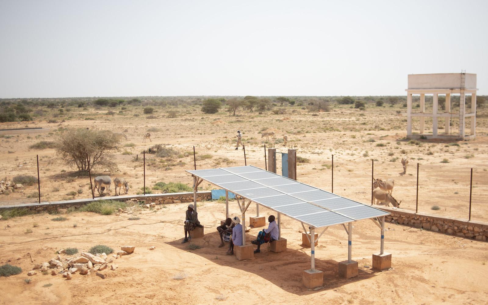 People sit in shade of solar panel
