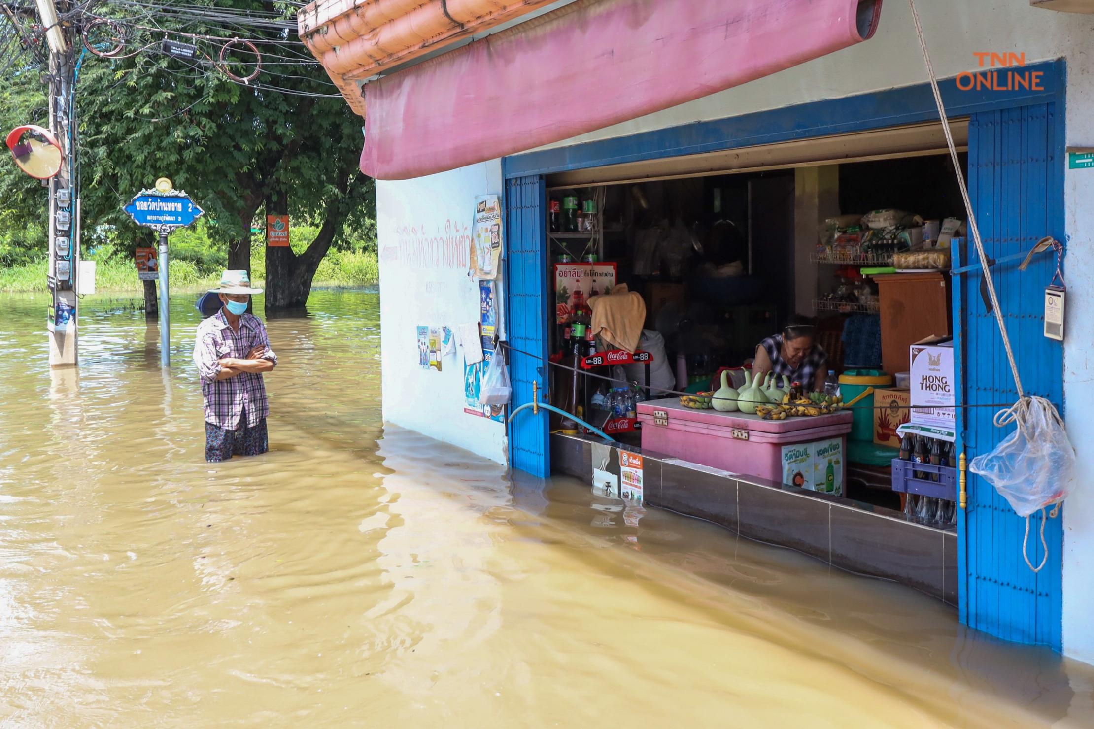 Man wearing mask stands in deep flood water outside shop