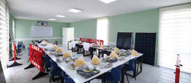 An empty meeting room with a table in the middle and solar panels on the background. Workers uniforms are neatly stacked in front of every chair, on the table.