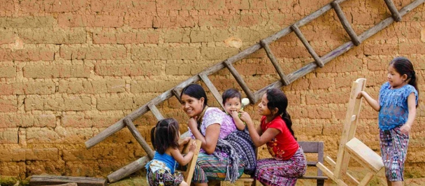 Guatemala family A woman and five children play together near a rustic wall and a wooden ladder.