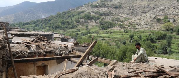 UNDP Afghanistan A man kneels on the ground looking out at a destroyed building with mountainous landscape in the background