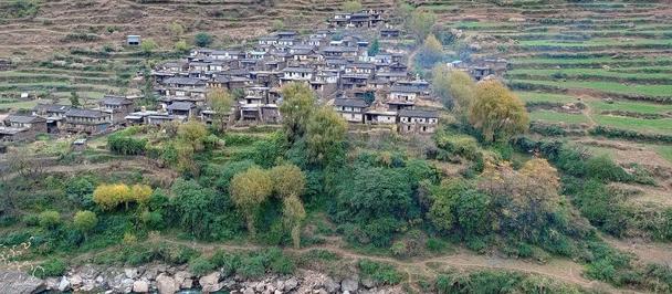 Hillside village with pastel houses atop terraced slopes along a rocky coastline and blue sea.
