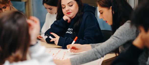 Woman sitting at a desk surrounded by students.