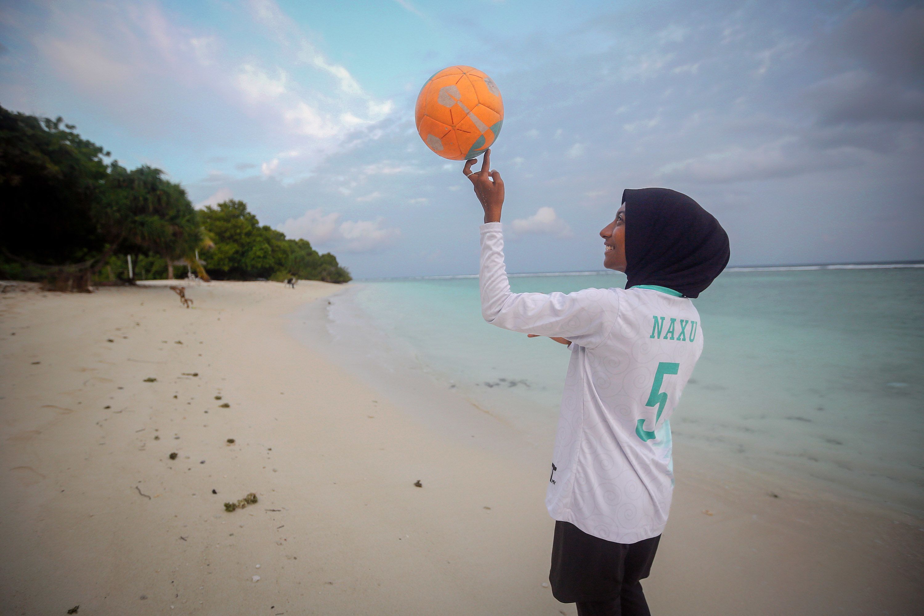 A young girl spinning a basketball on a beach