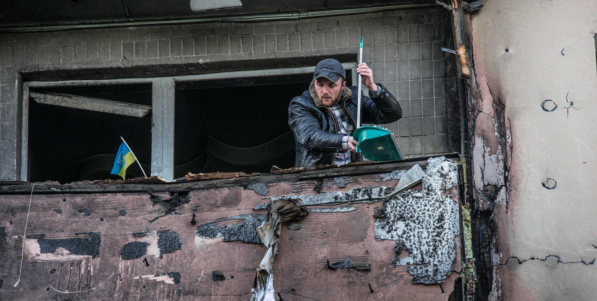 A man sweeps rubble from the balcony of an apartment damaged by shelling.