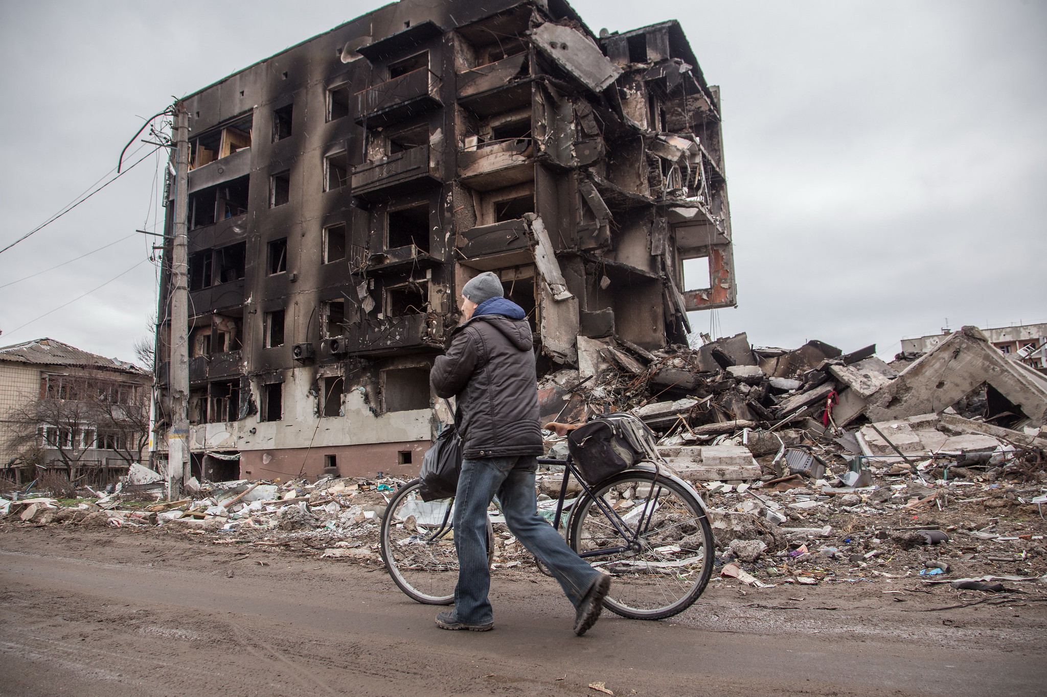A man pushes a bike past a destroyed building.