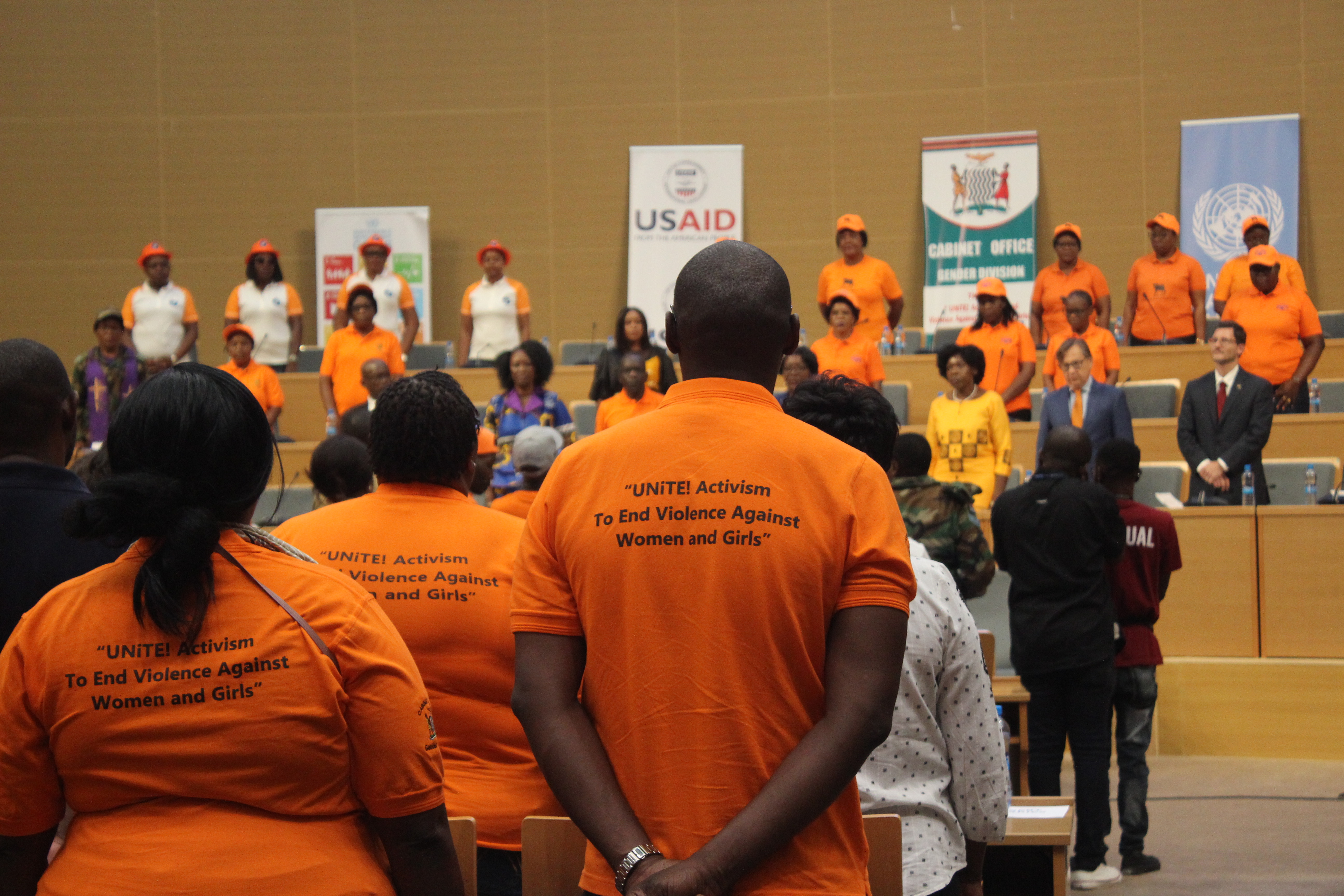 A man wearing a orange t-shirt that reads "UNiTE: Activism to End Violence Against Women and Girls"