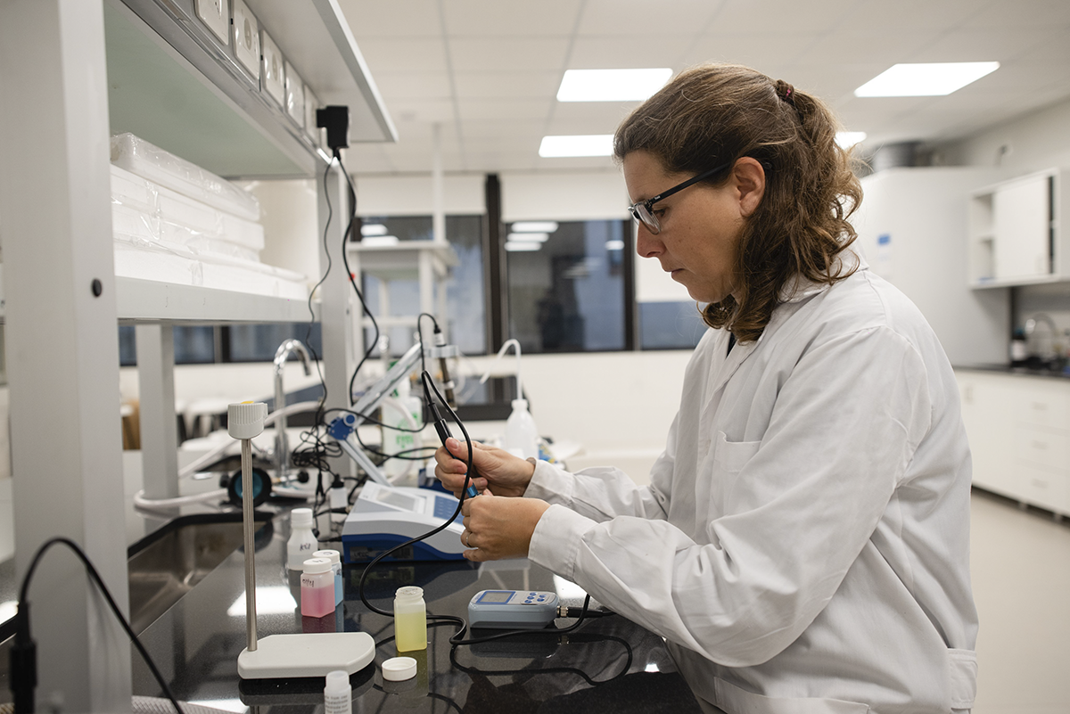 Mujer científica, sentada de túnica, en laboratorio, concentrada trabajando