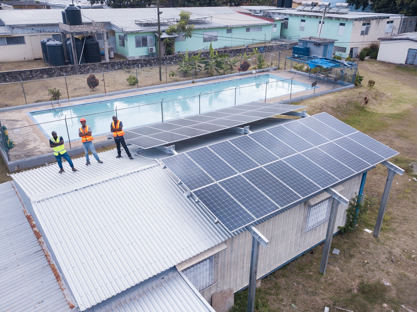 Three maintenance workers posing with solar panels installed on the roof of Sir John Golding Rehabilitation Center in St. Andrew, Jamaica.