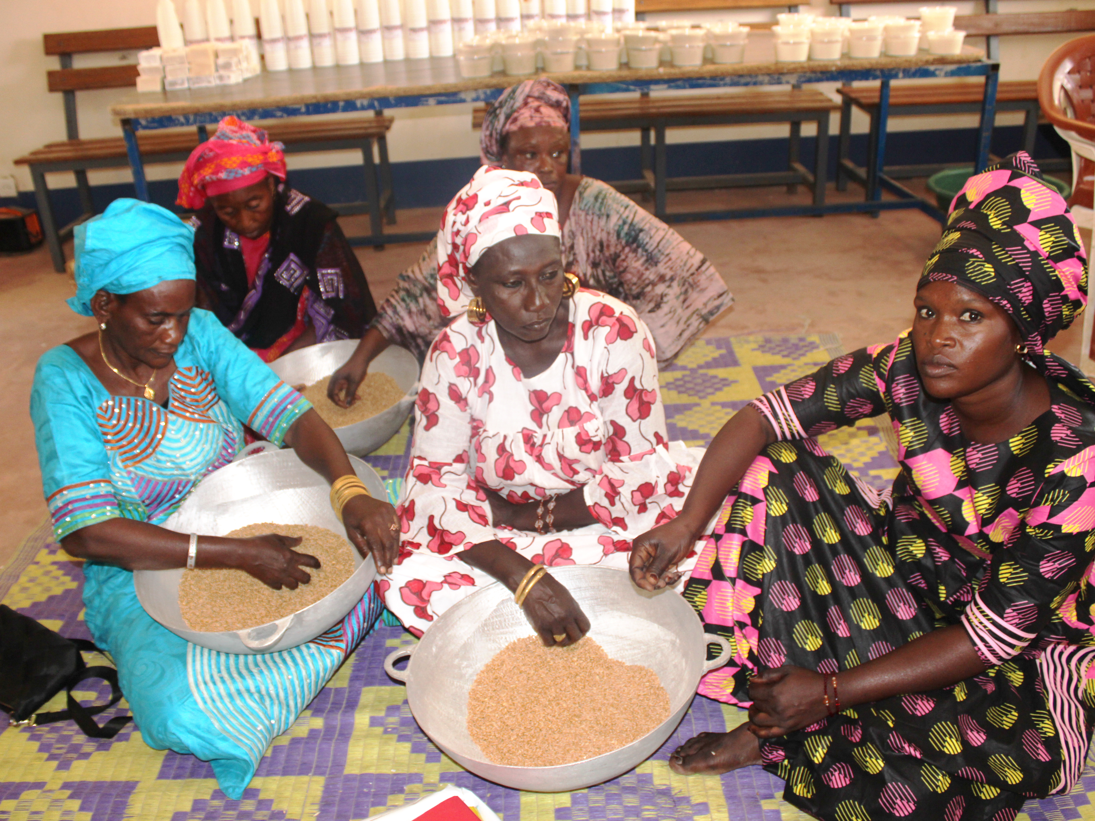Quatre femmes portant sur leurs genoux des calebasses remplies de blé pour le transformé