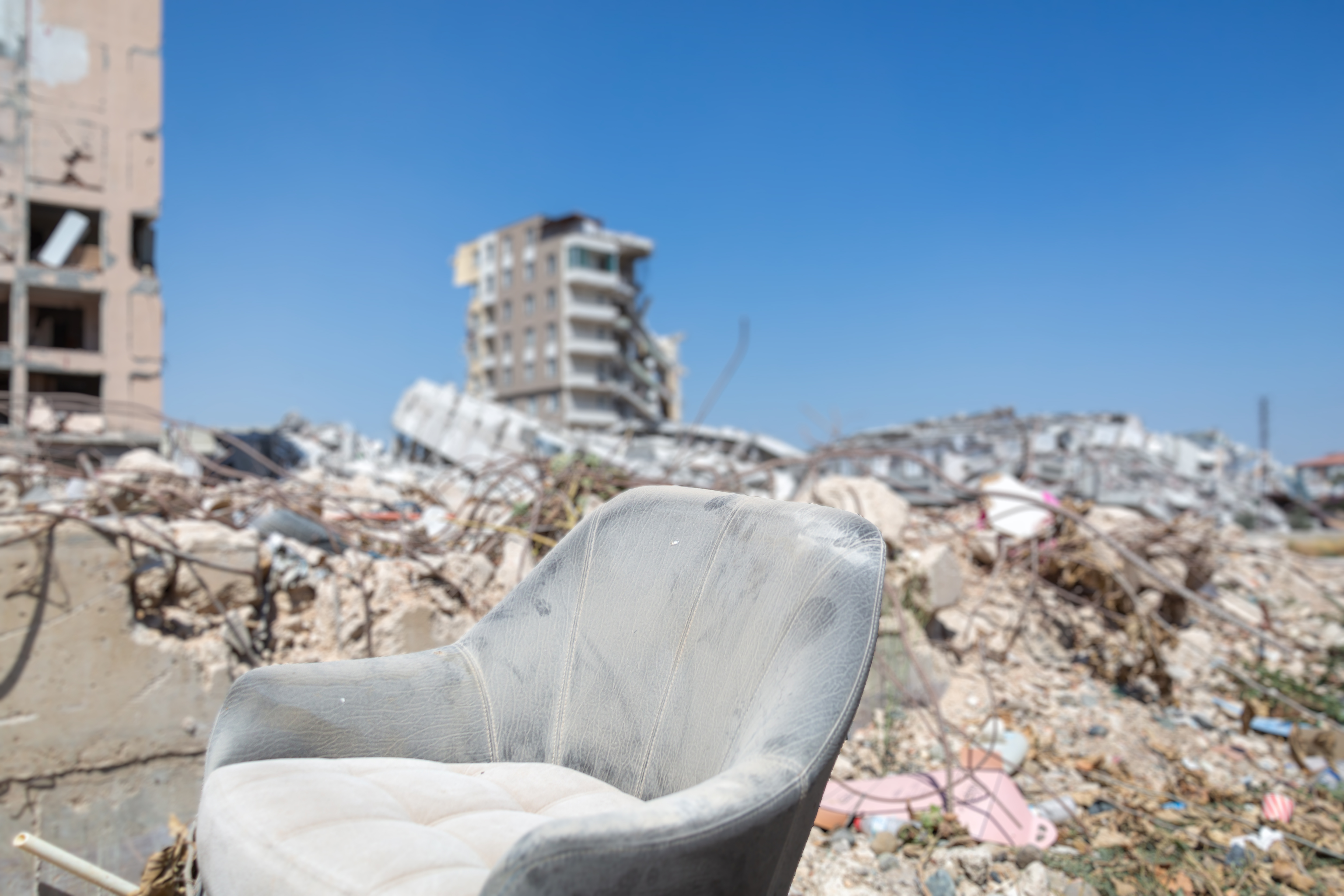 A dusty armchair sitting in front of the collapsed buildings with earthquake debris on the background.