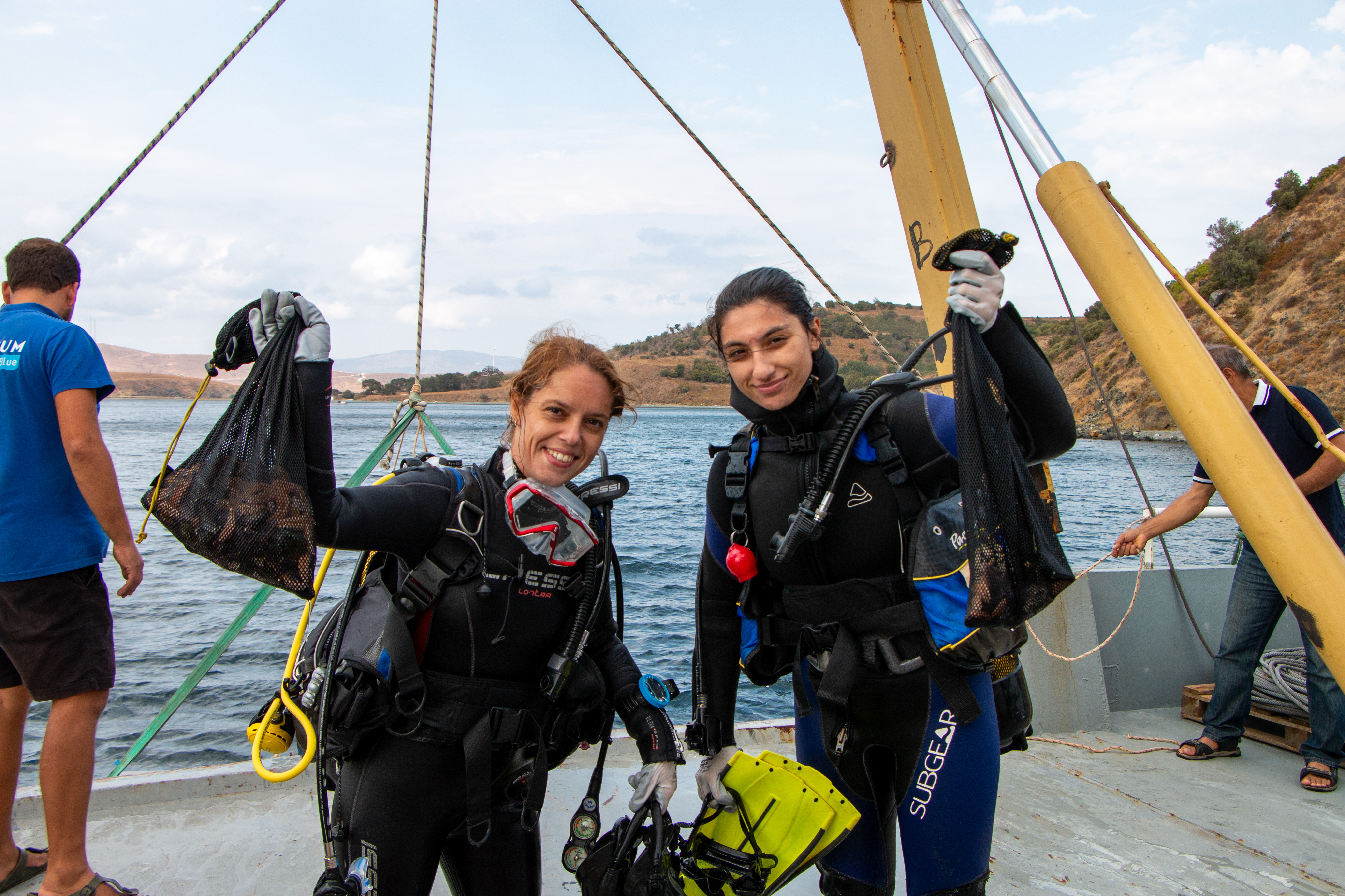 Two young woman in scuba gear smiling, looking at the camera holding underwater nets with starfish inside
