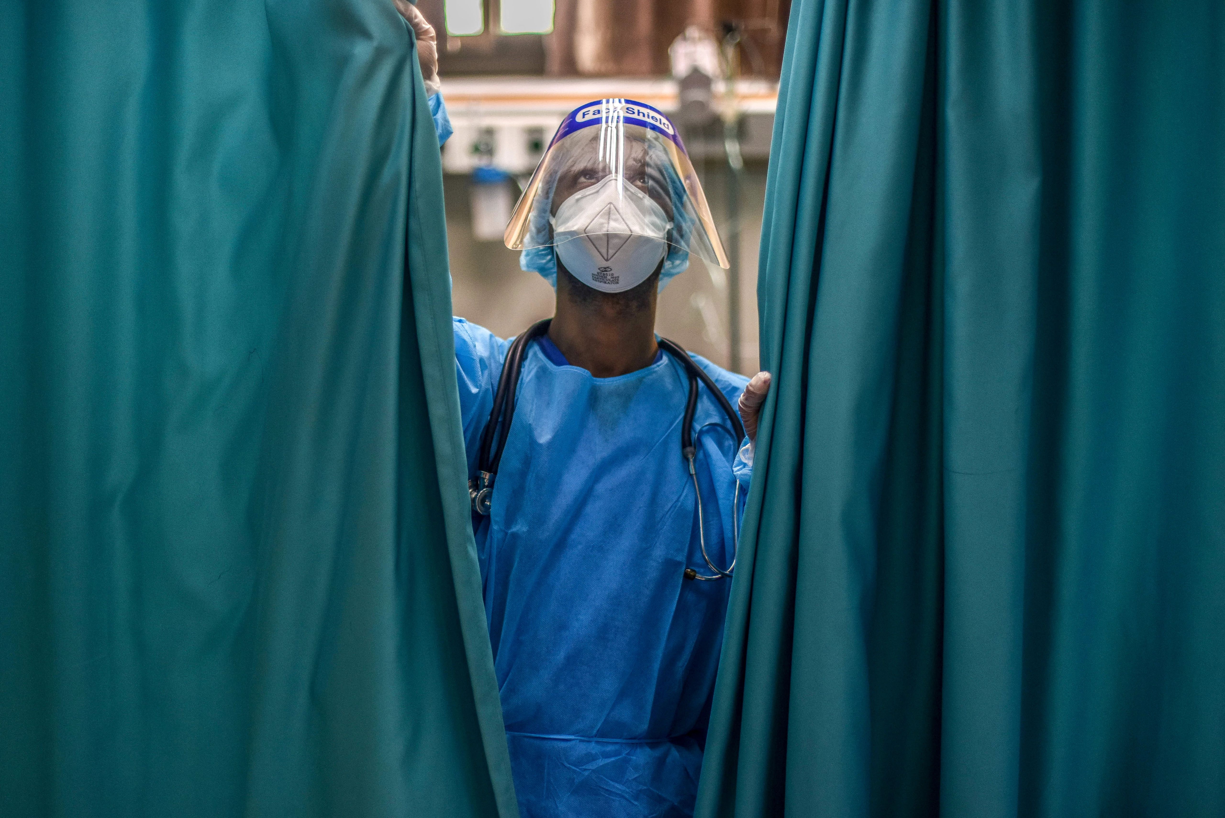 Person in a surgical mask and scrubs stands next to curtains