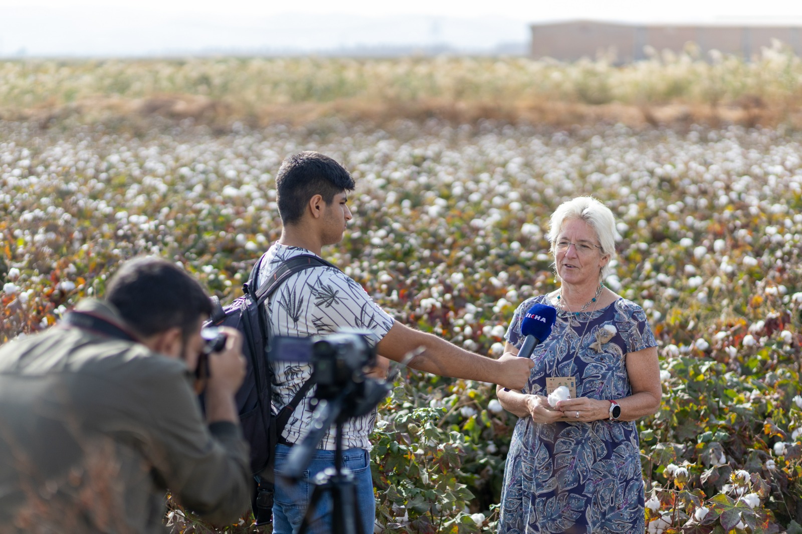 UNDP Türkiye Resident Representative Louisa Vinton standing in front of a cotton field with a reporter pointing a microphone at her and another reporter behind the camera
