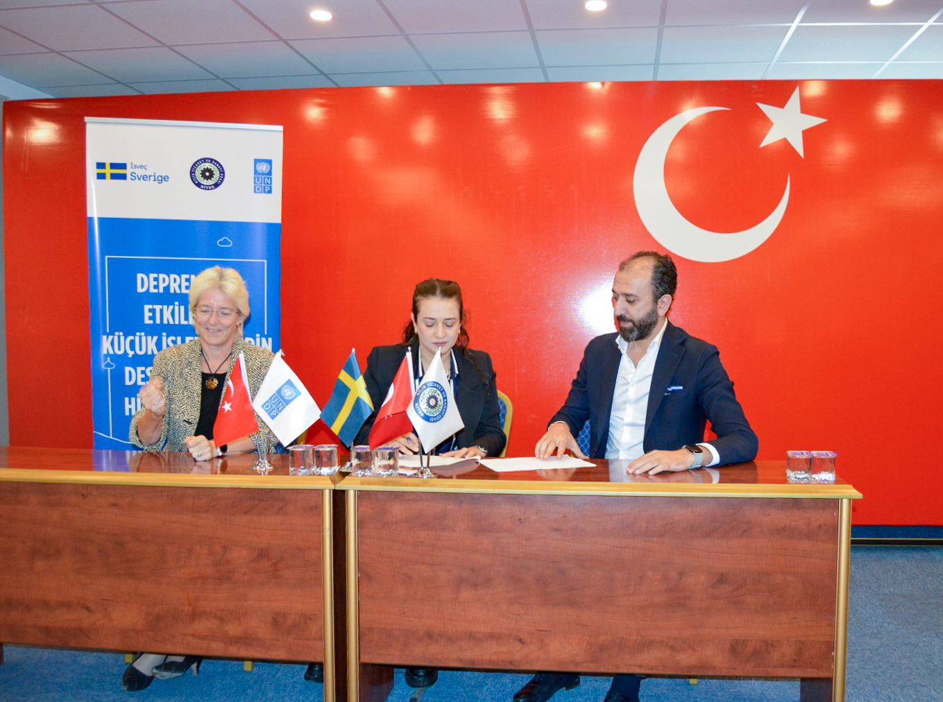 UNDP Türkiye Resident Representative Louisa Vinton and head of Kilis Chamber of Commerce sitting in front of a desk during the signature ceremony with Turkish flag on the background.