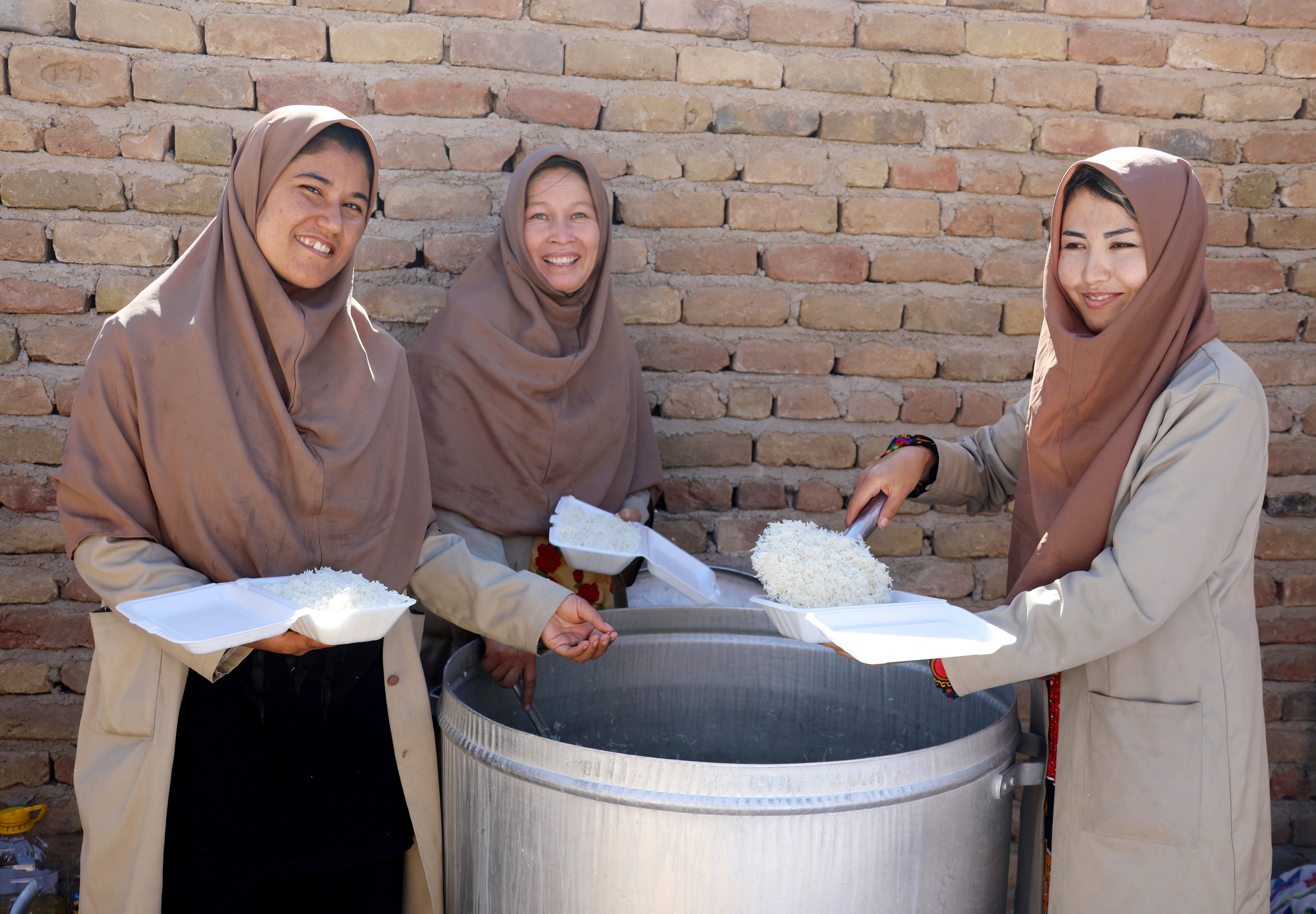 Three women in abeyas dish rice from a large pot.