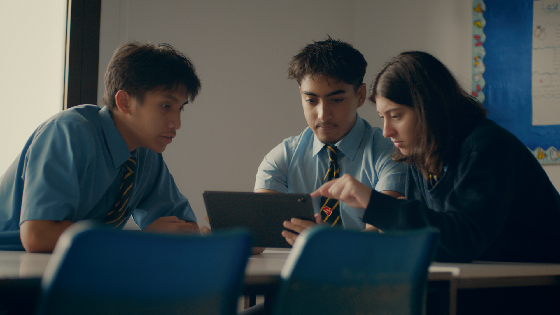 Three students look at a laptop