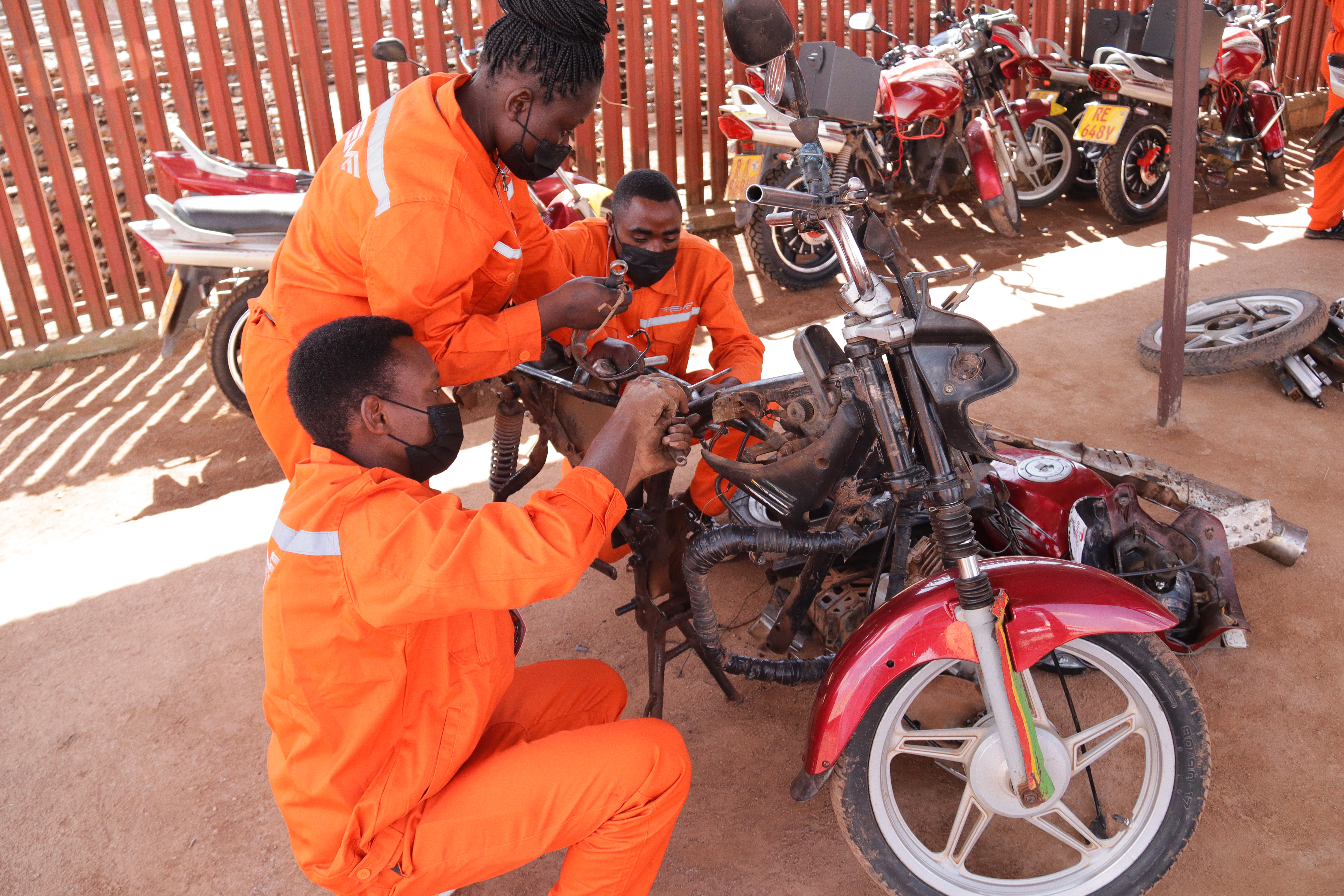Men in orange overalls work on motorbike