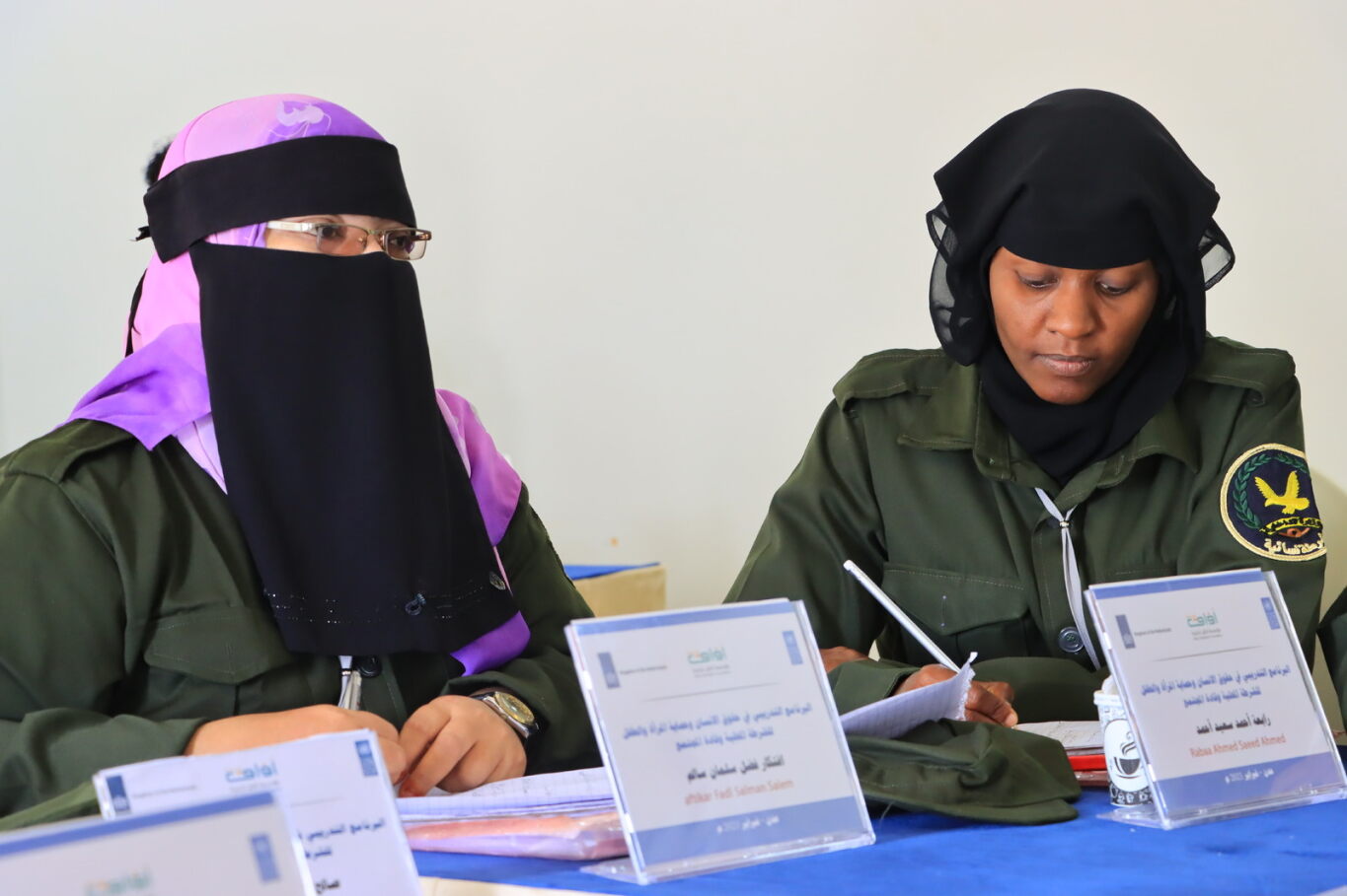 Woman in abeya sits next to woman in police uniform