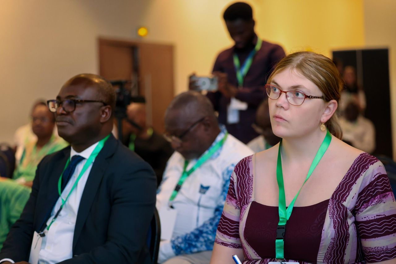A diverse group of attendees sitting in a conference setting, focused on a speaker.