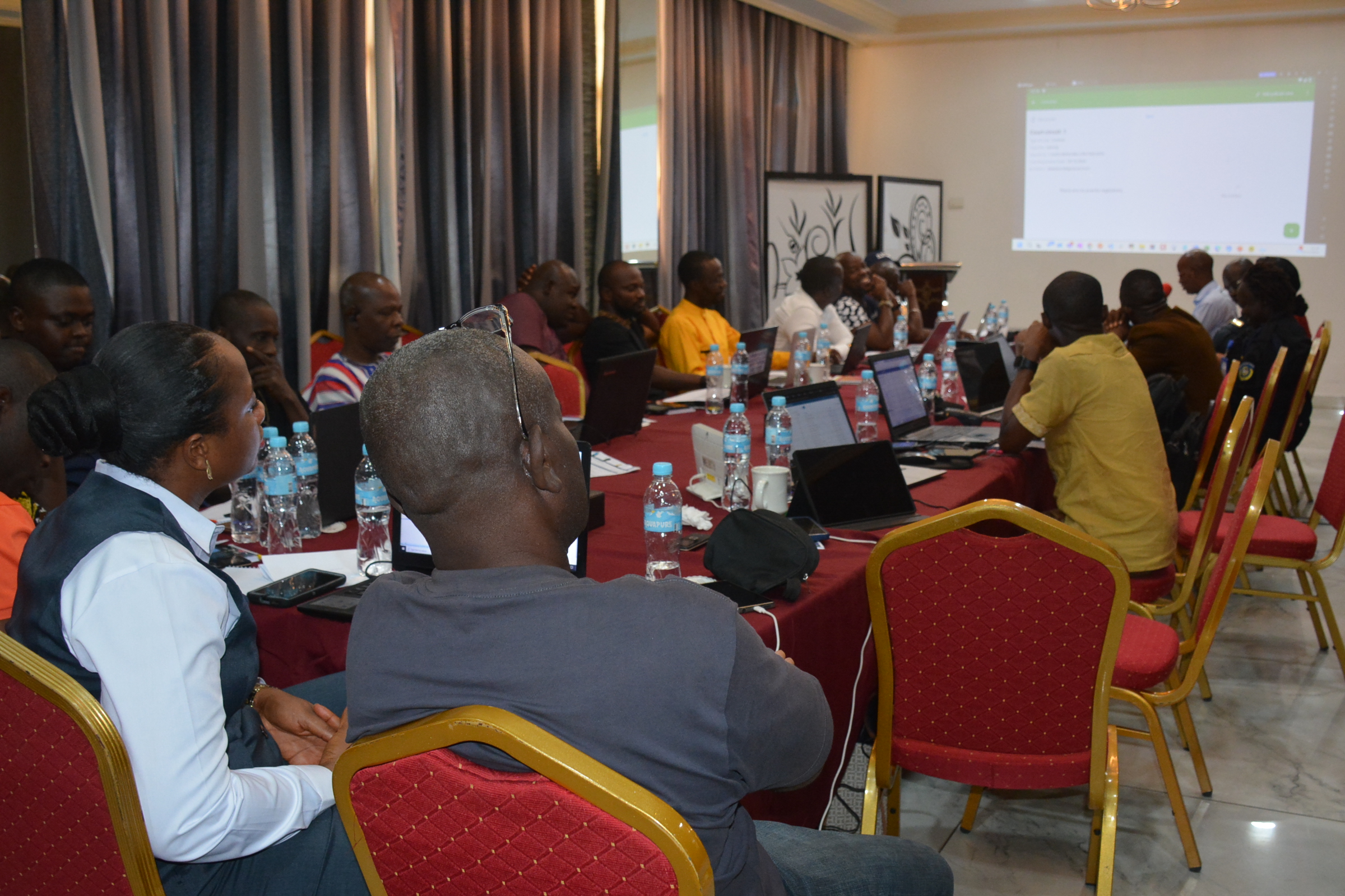 Participants engaged in a meeting around a conference table, with laptops and presentation screen.