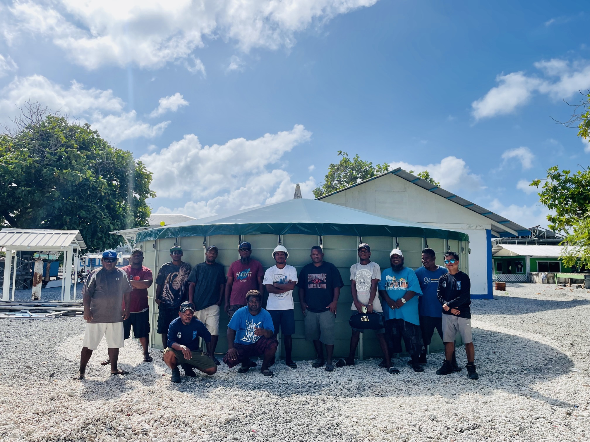 Group of men standing in front of a circular building under a blue sky with clouds.