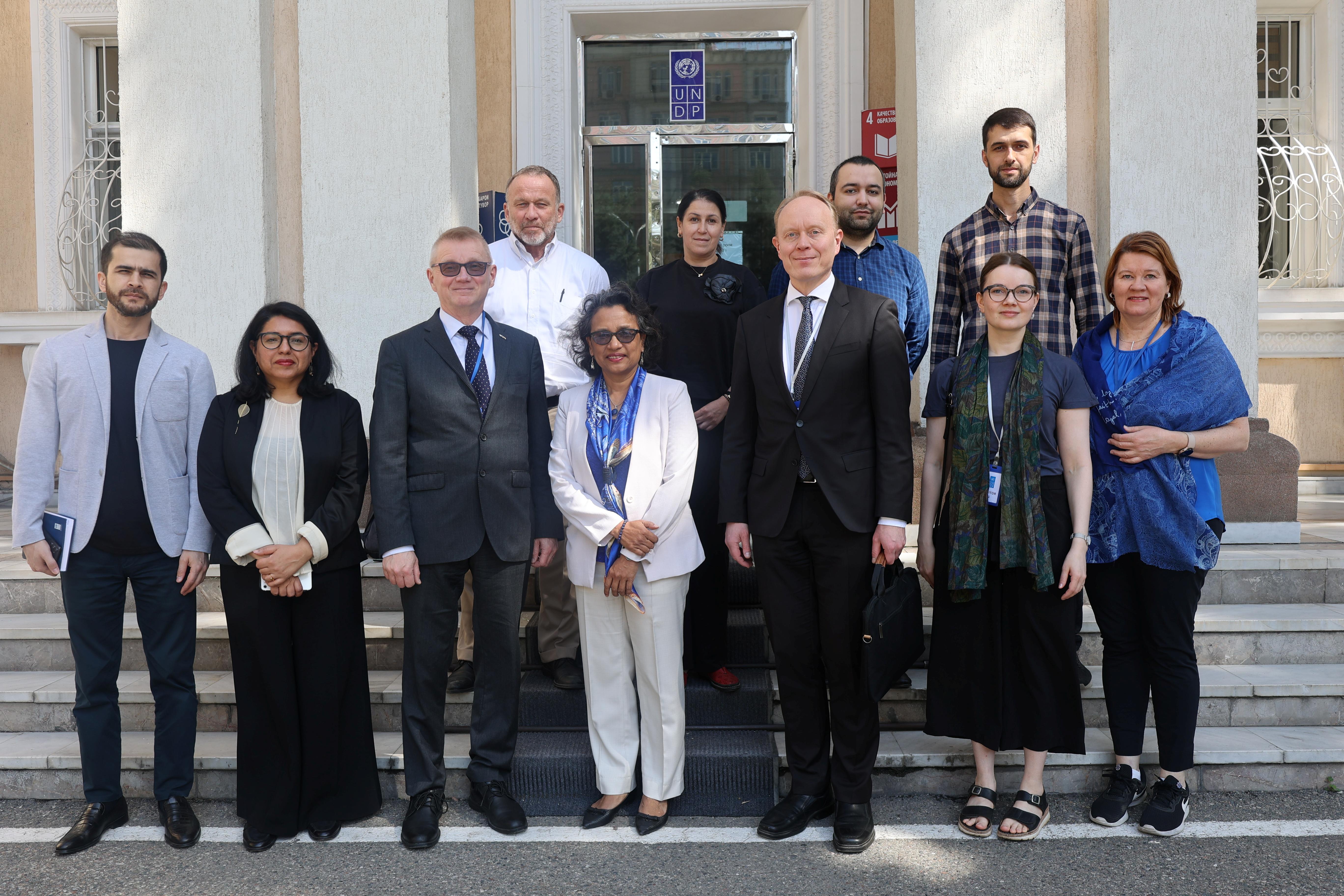 A diverse group of eleven people poses for a photo outside a building, smiling and standing on steps.
