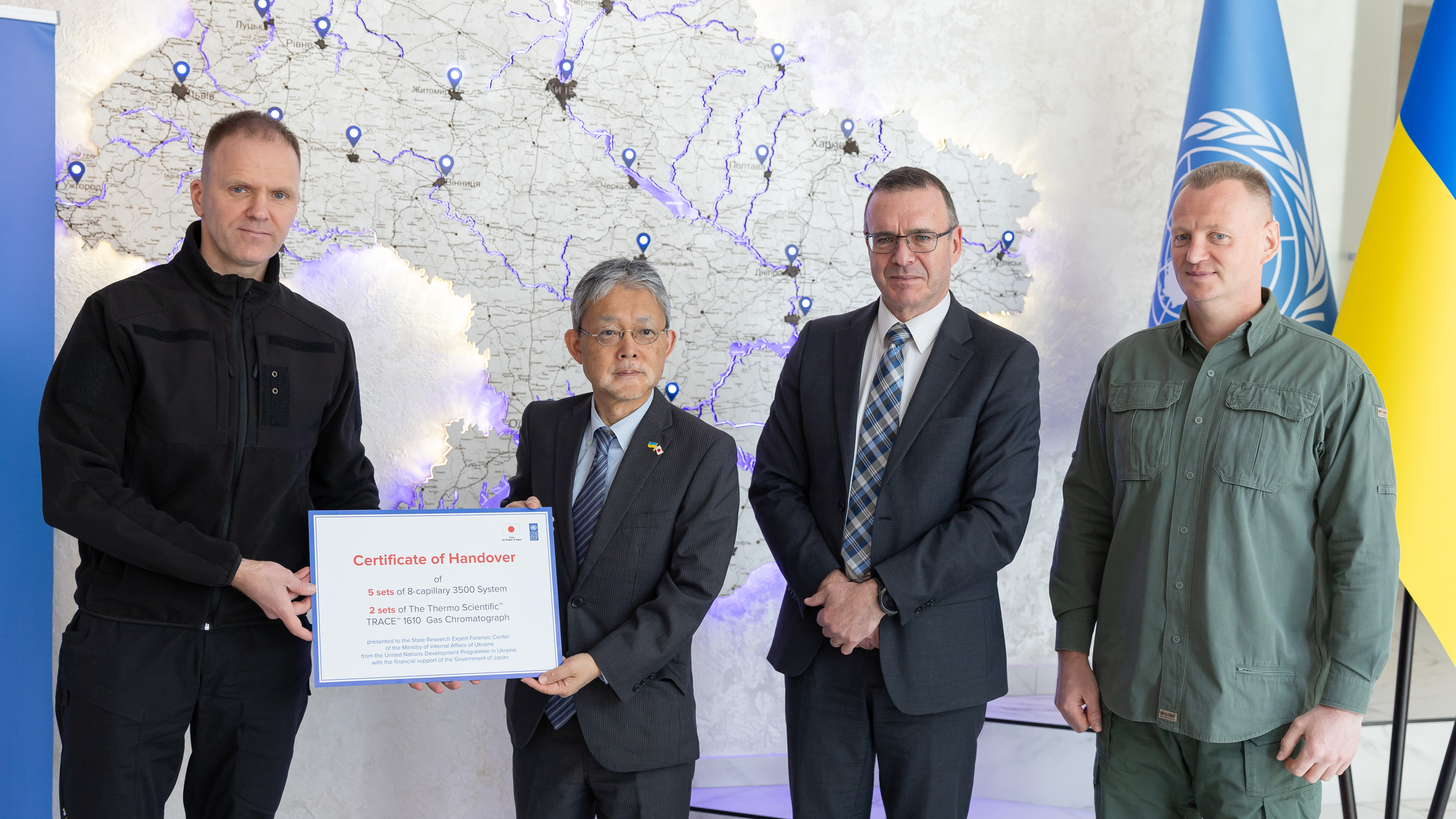 Four individuals in professional attire pose together, holding a certificate in front of a map.