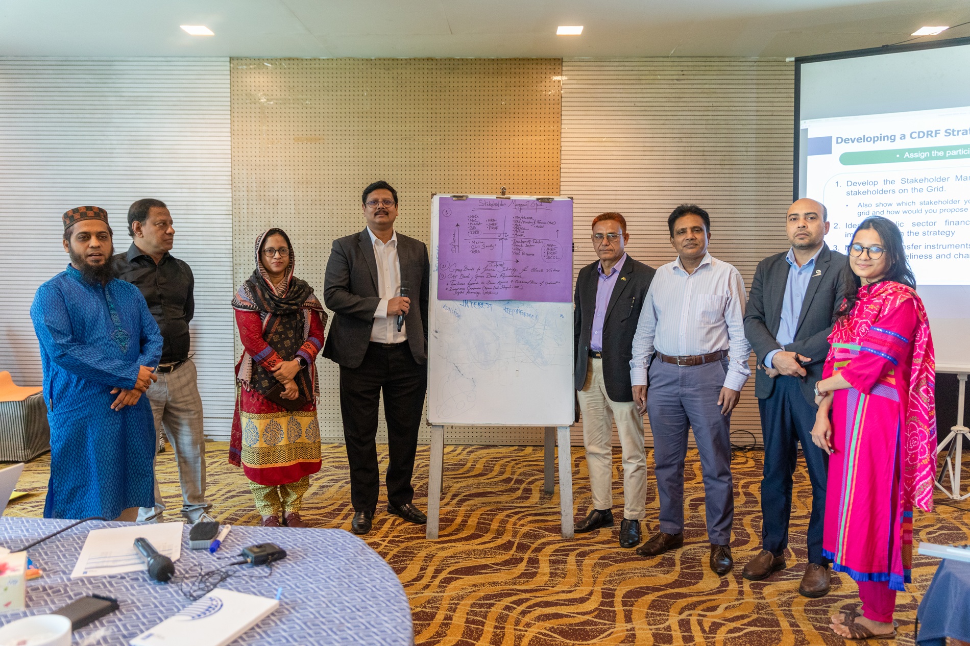 A group of seven people standing around a flip chart in a conference room setting.
