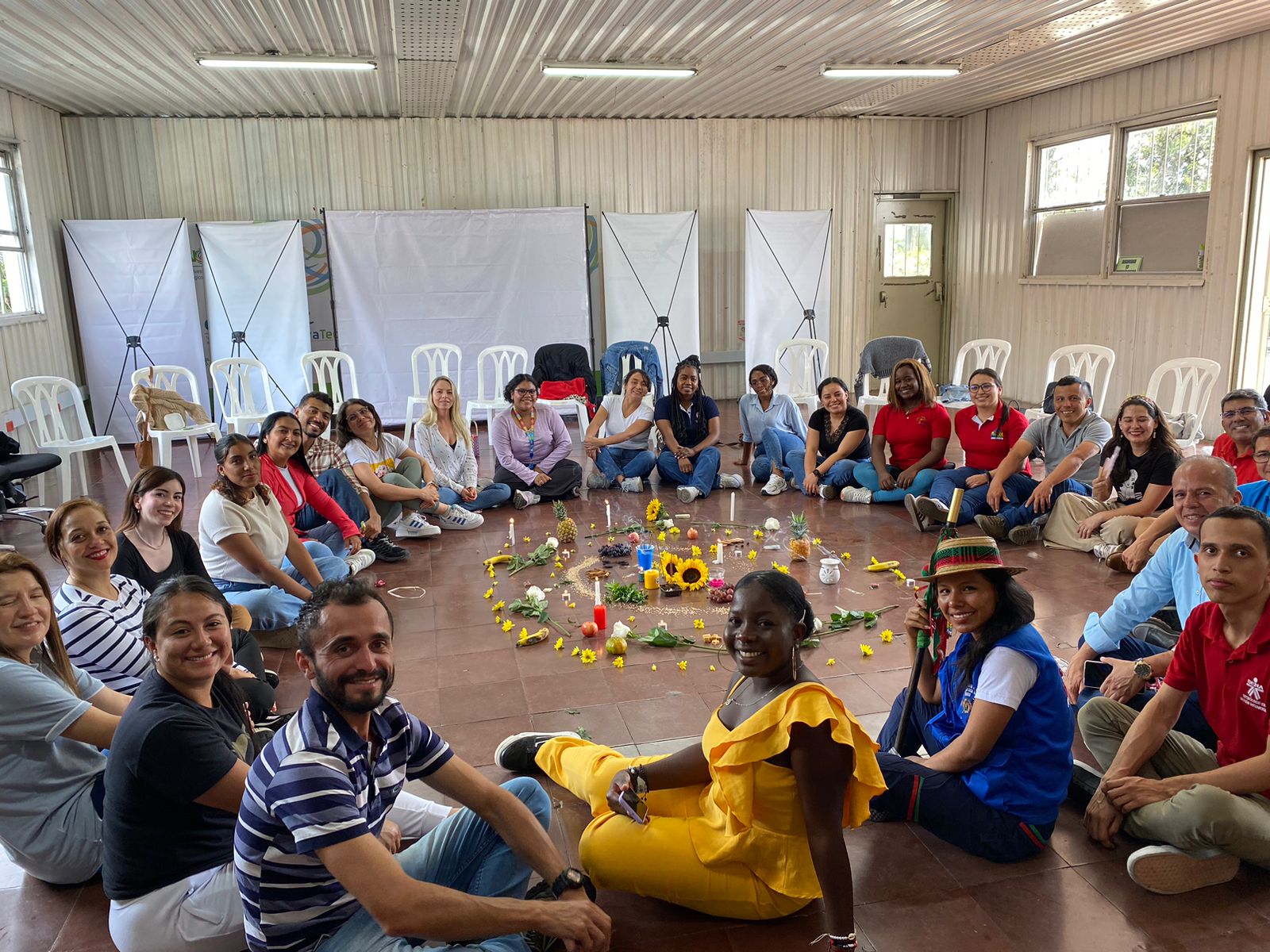 Group of diverse individuals seated in a circle around colorful decorations on the floor.