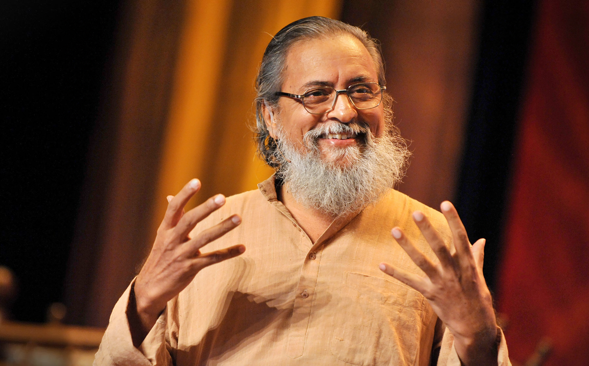 Smiling man with a beard enthusiastically gesturing with his hands, wearing an orange shirt.