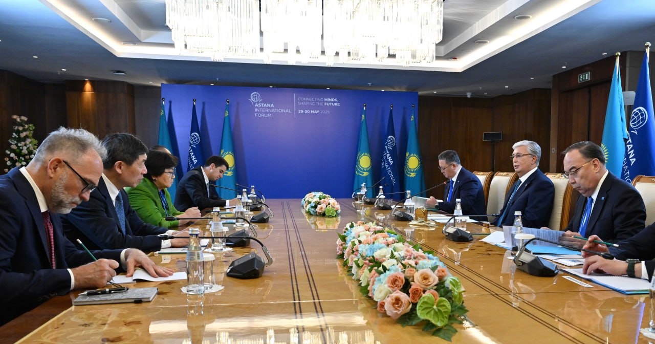 A group of officials in formal attire seated around a conference table with a floral centerpiece.