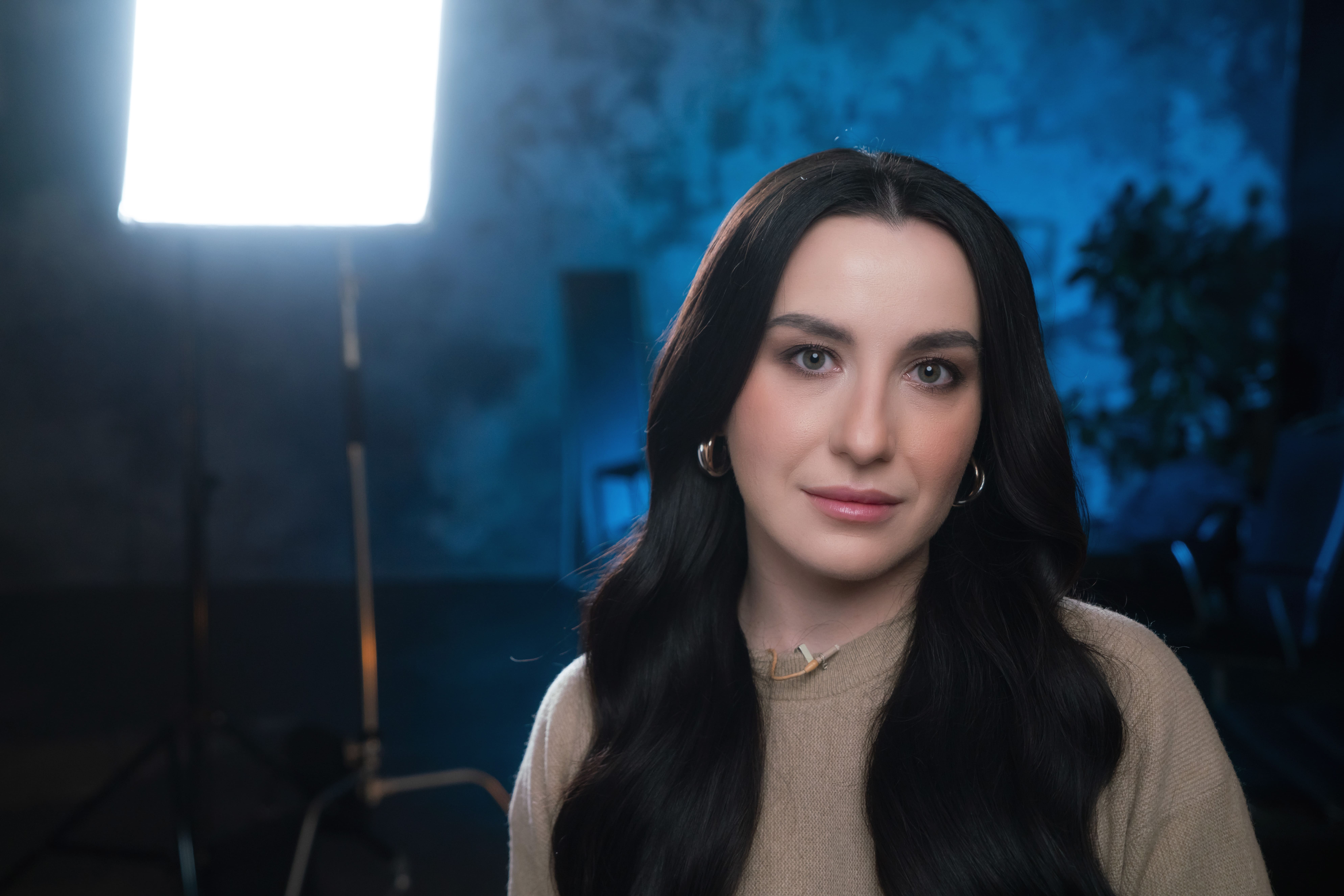 A woman with long dark hair poses slightly to the side, framed by blue lighting.