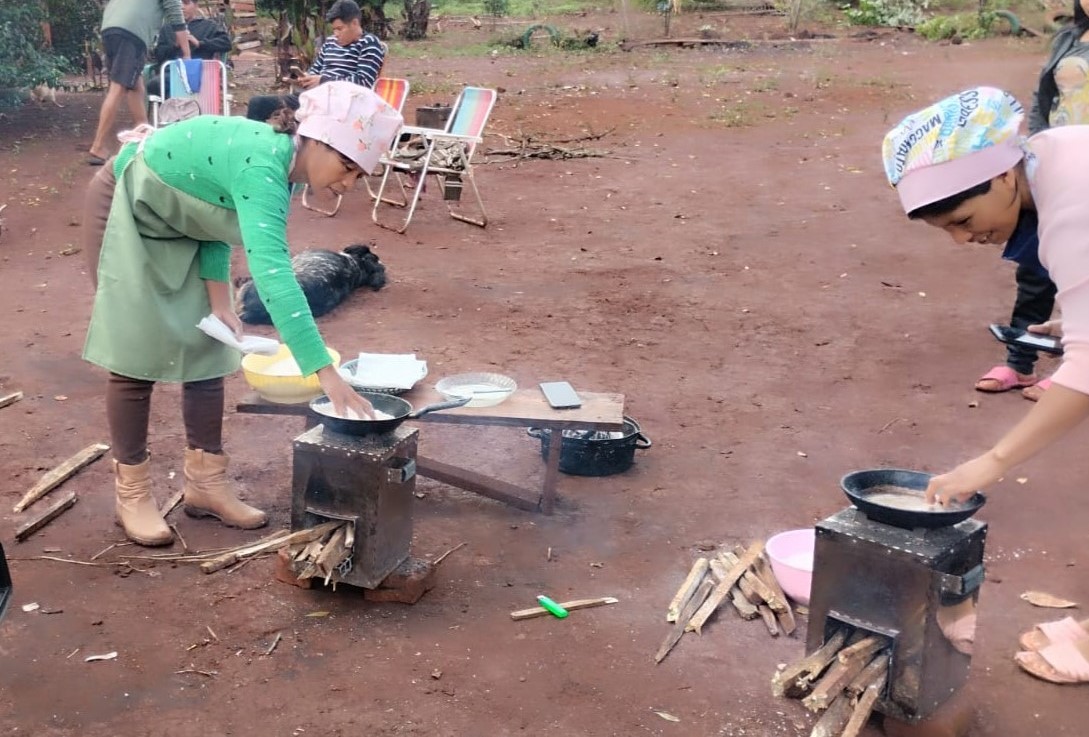 Dos mujeres cocinando en cocinas ecológicas, en un entorno natural con suelo de tierra.