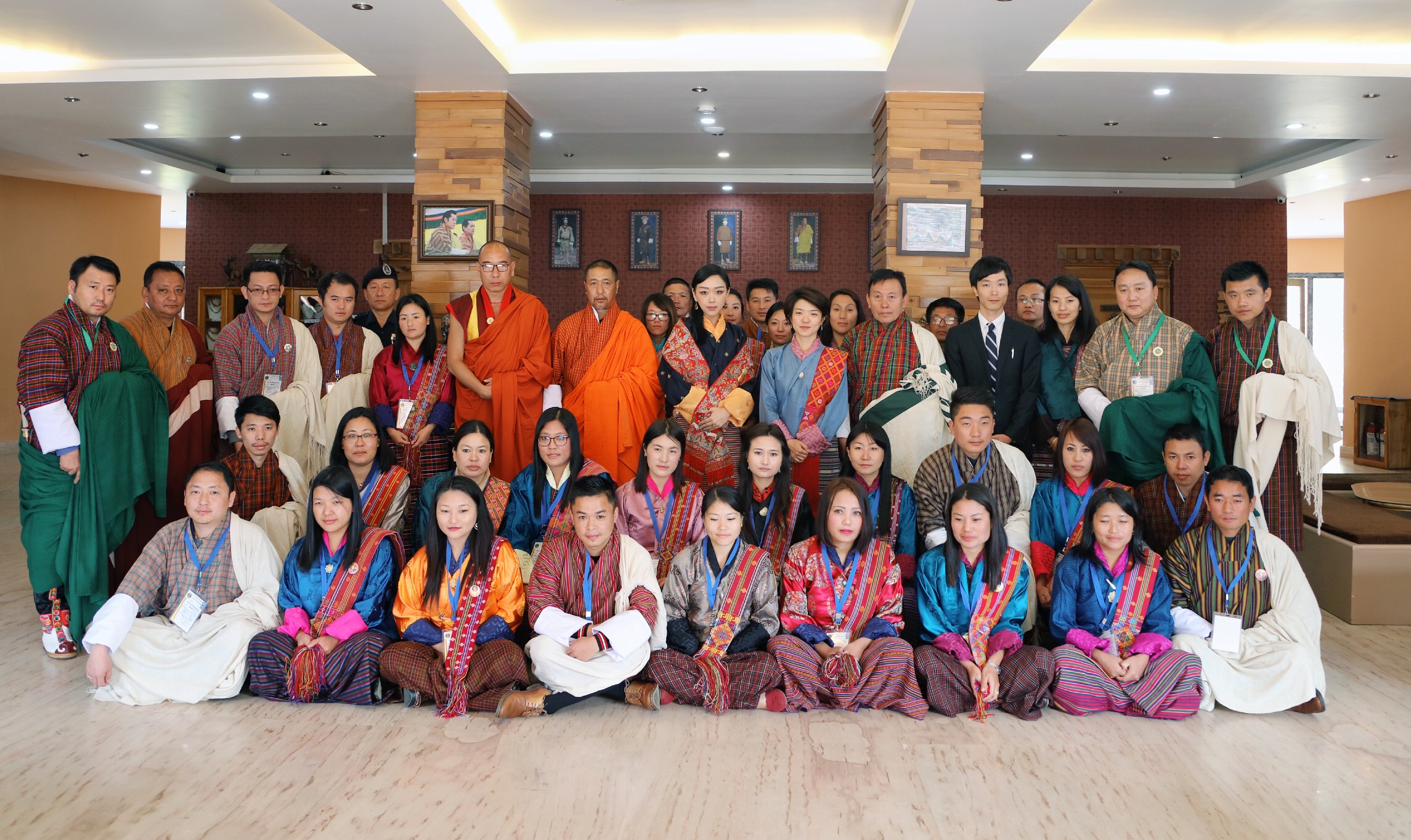 A large group of individuals in traditional attire poses together in a spacious indoor setting.