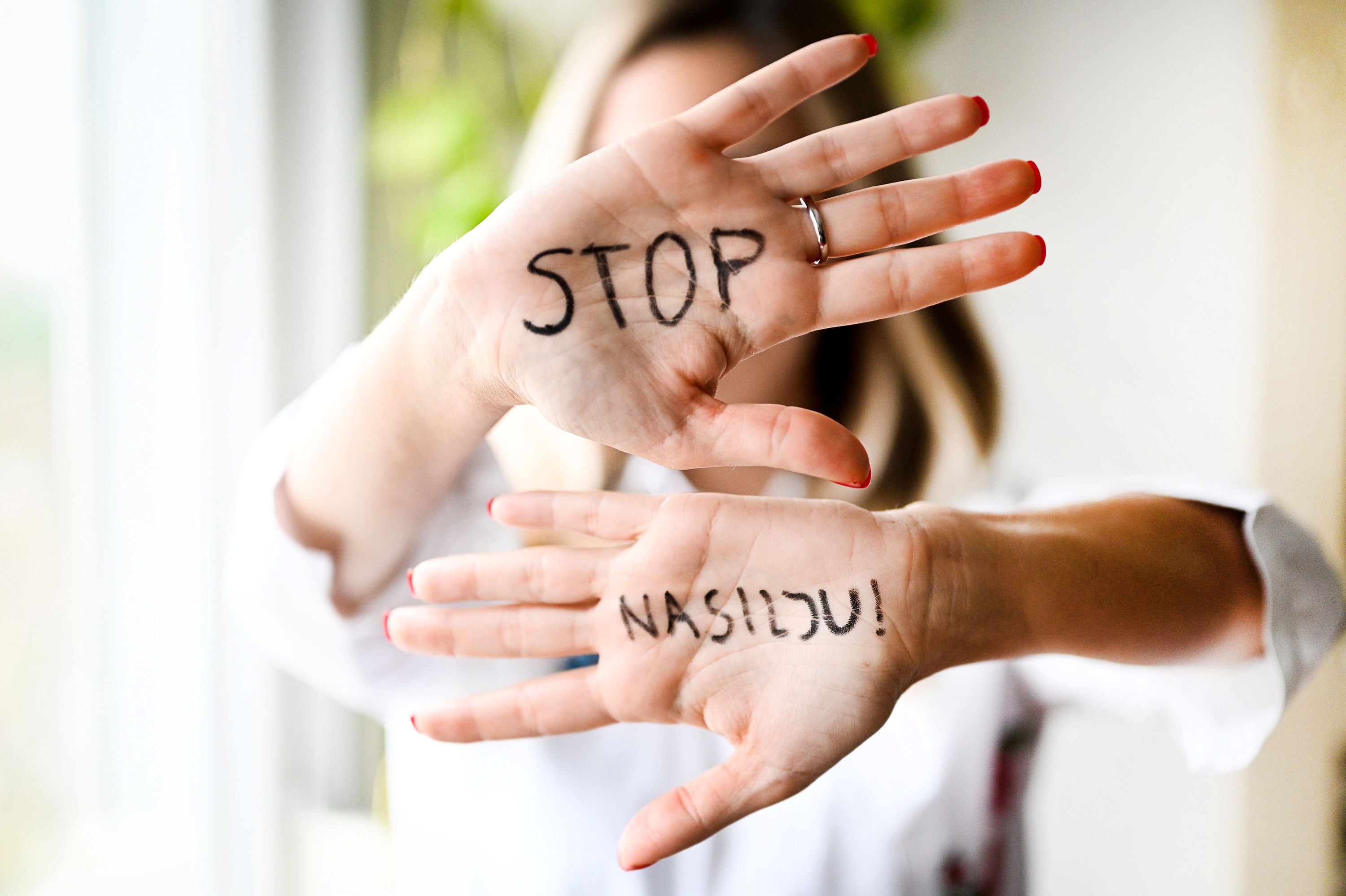A person holds up both hands, each with words written: "STOP" and "NASTIDU!"