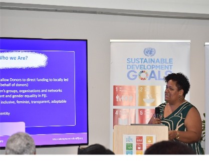 A presenter speaks at a seminar, with a display of Sustainable Development Goals behind her.