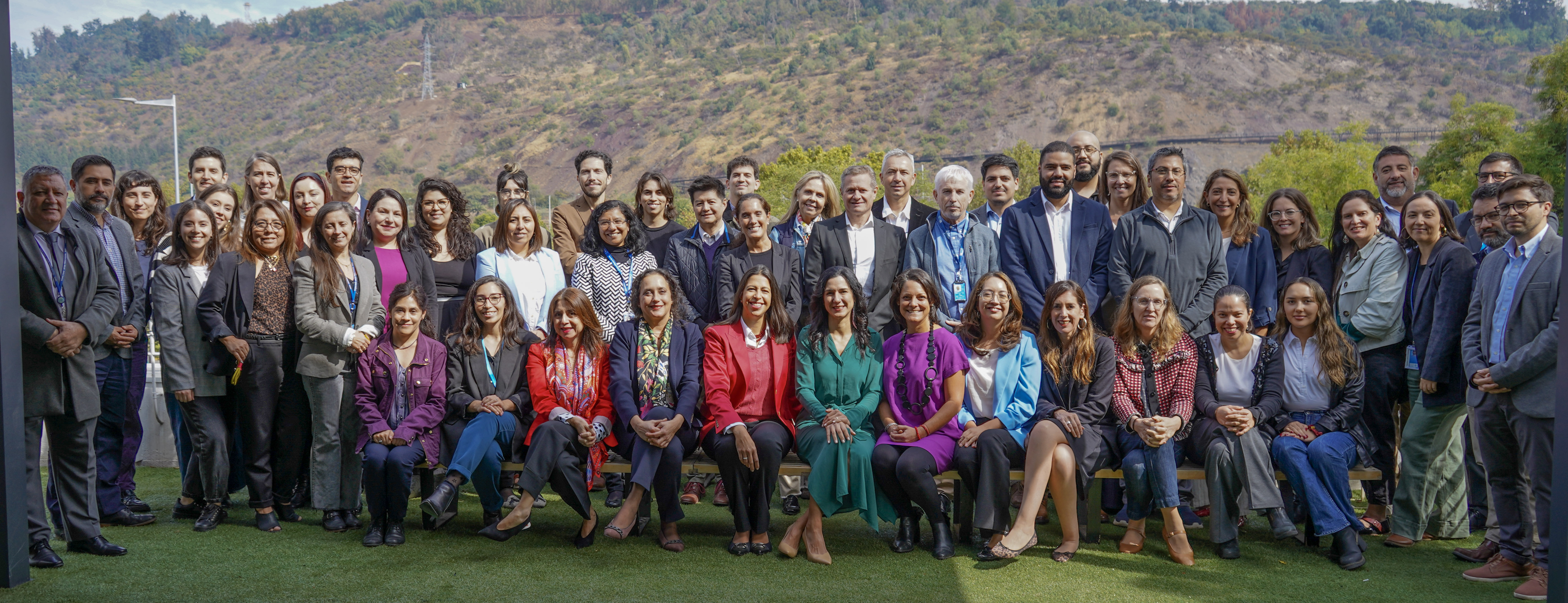 A large group of professionals posing outdoors with a mountainous backdrop.