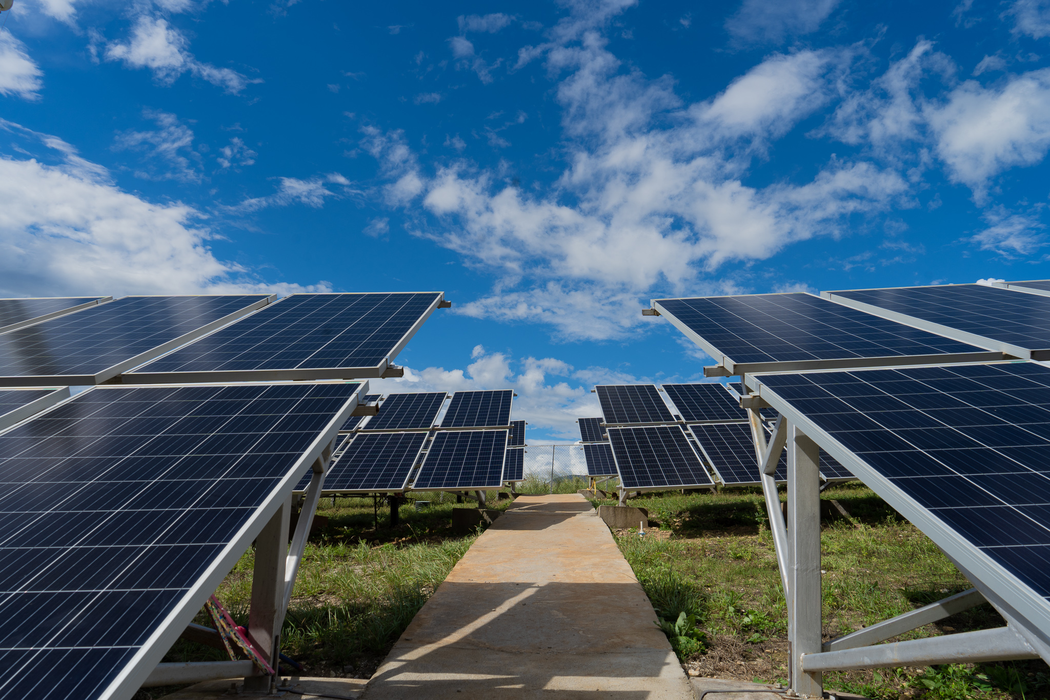 Solar panels lined along a path under a bright blue sky with scattered clouds.