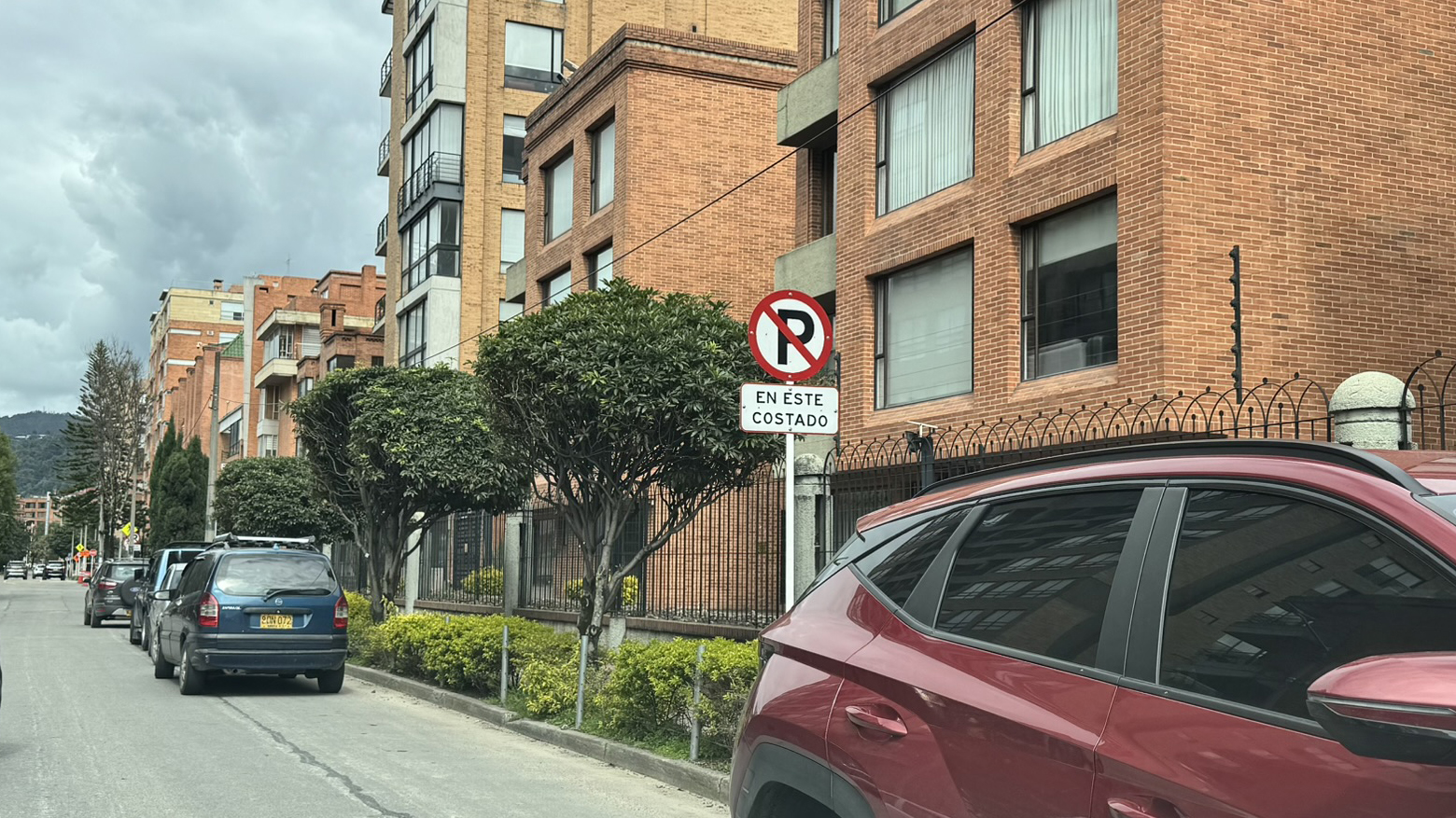 Street scene featuring parked cars alongside red brick buildings and a no-parking sign.