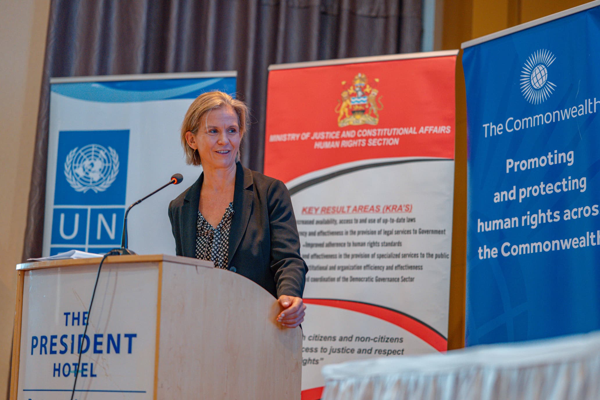 Woman speaking at a podium with banners in the background promoting human rights.