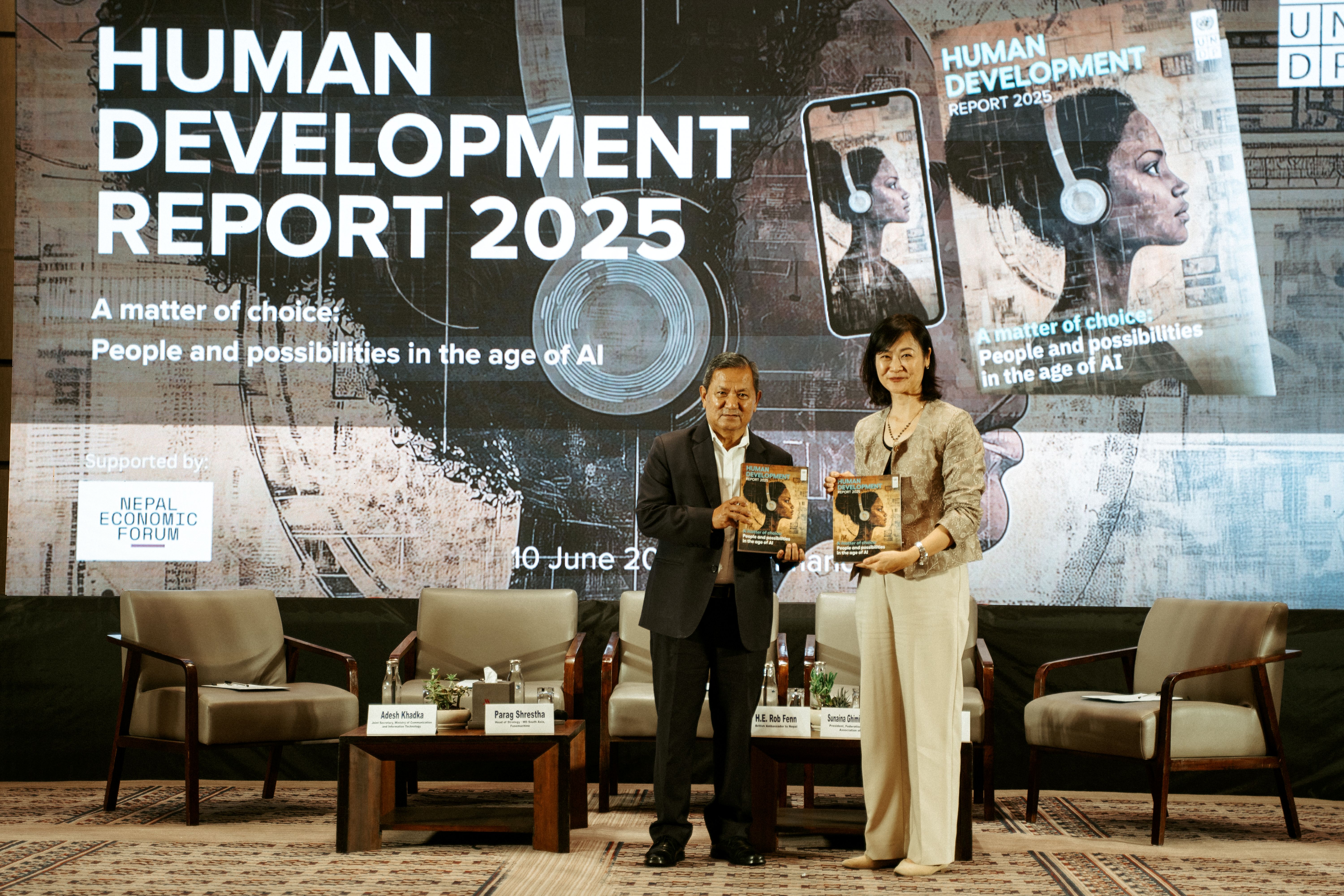 Two individuals holding a report on stage, with a large presentation backdrop.