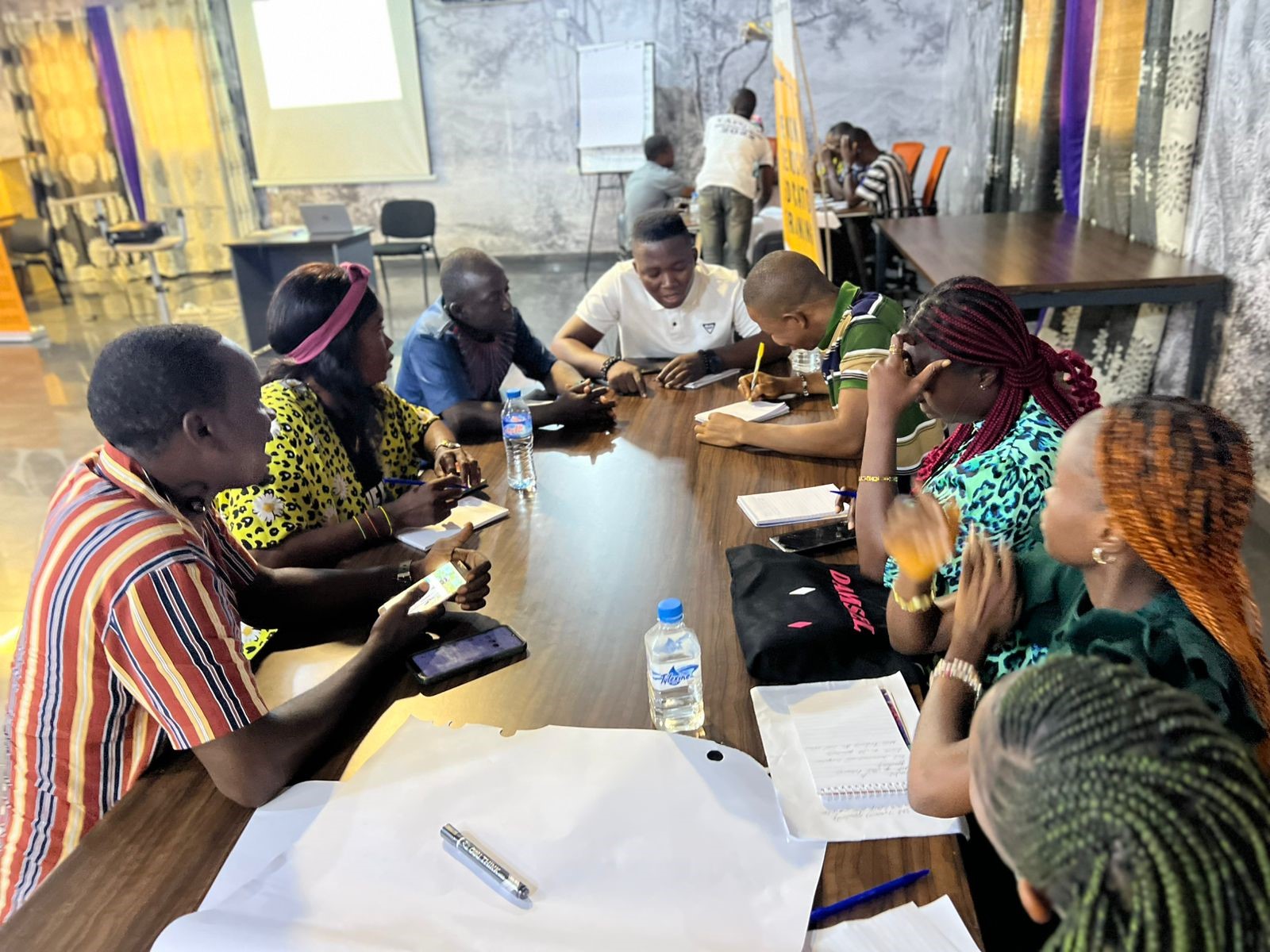 A group of diverse individuals engaged in discussion around a table, using phones.