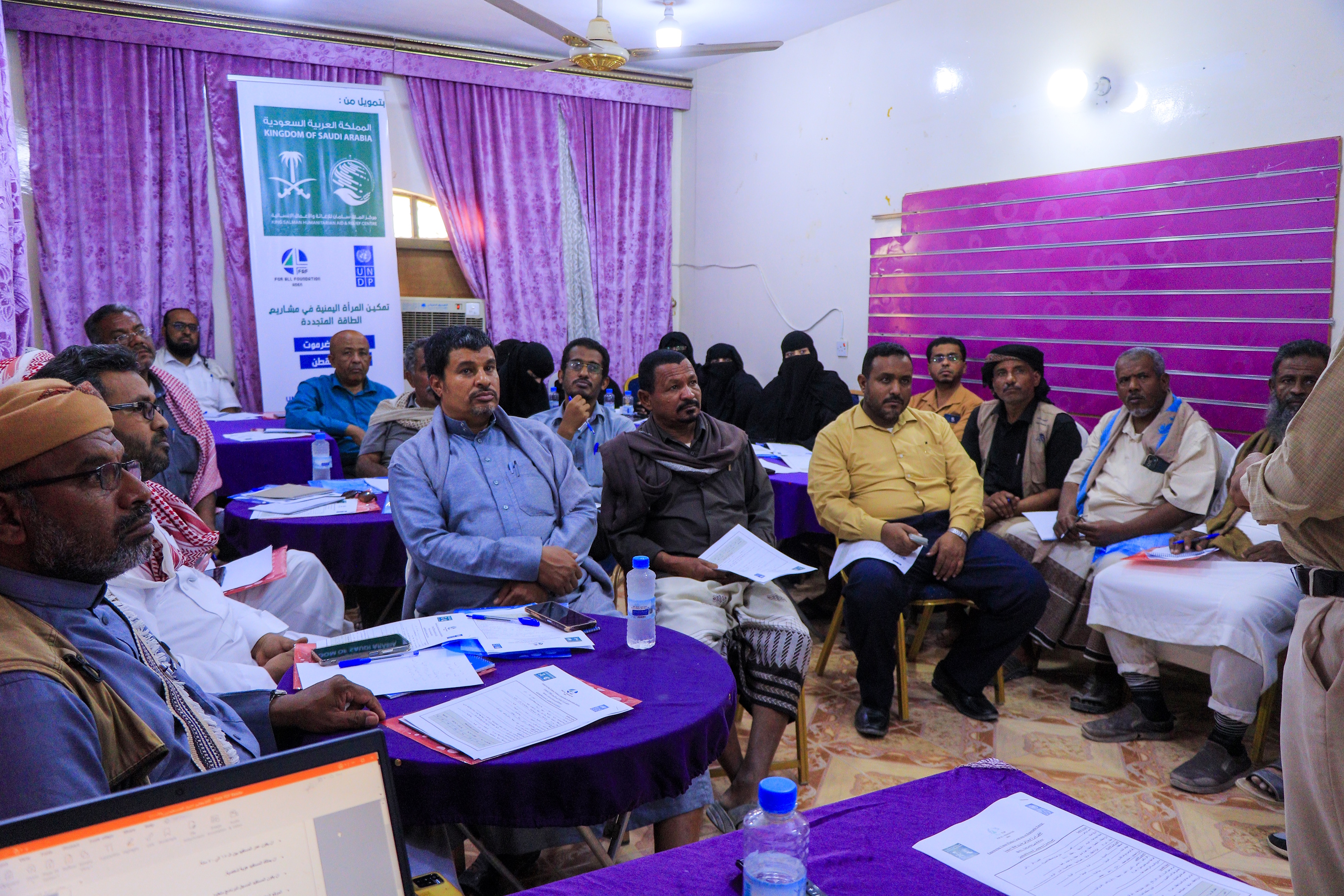 A group of people sitting in a brightly lit room, engaged in a discussion or presentation.