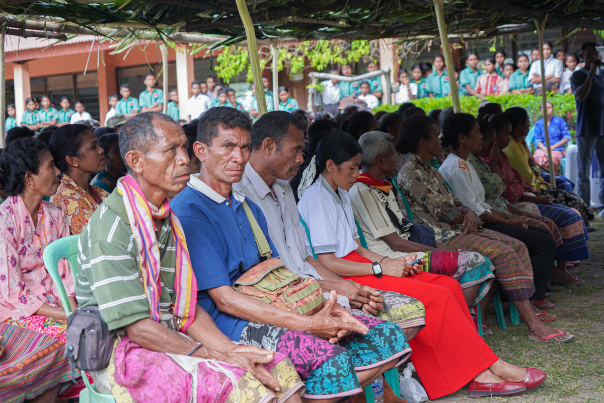A diverse group of seated people, dressed in colorful traditional attire, at an outdoor event.