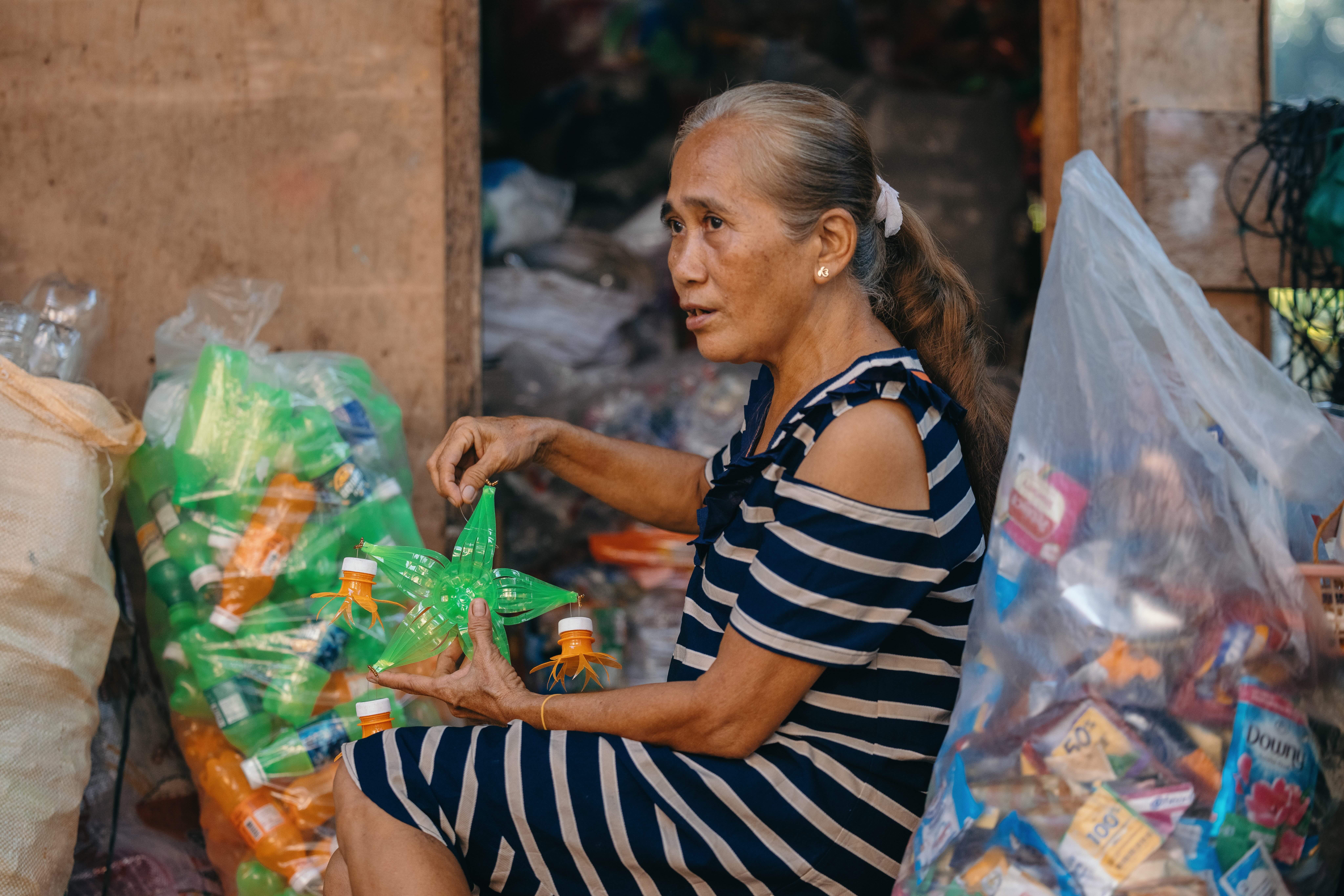 Elderly woman in a striped dress sorting through colorful plastic waste bags.