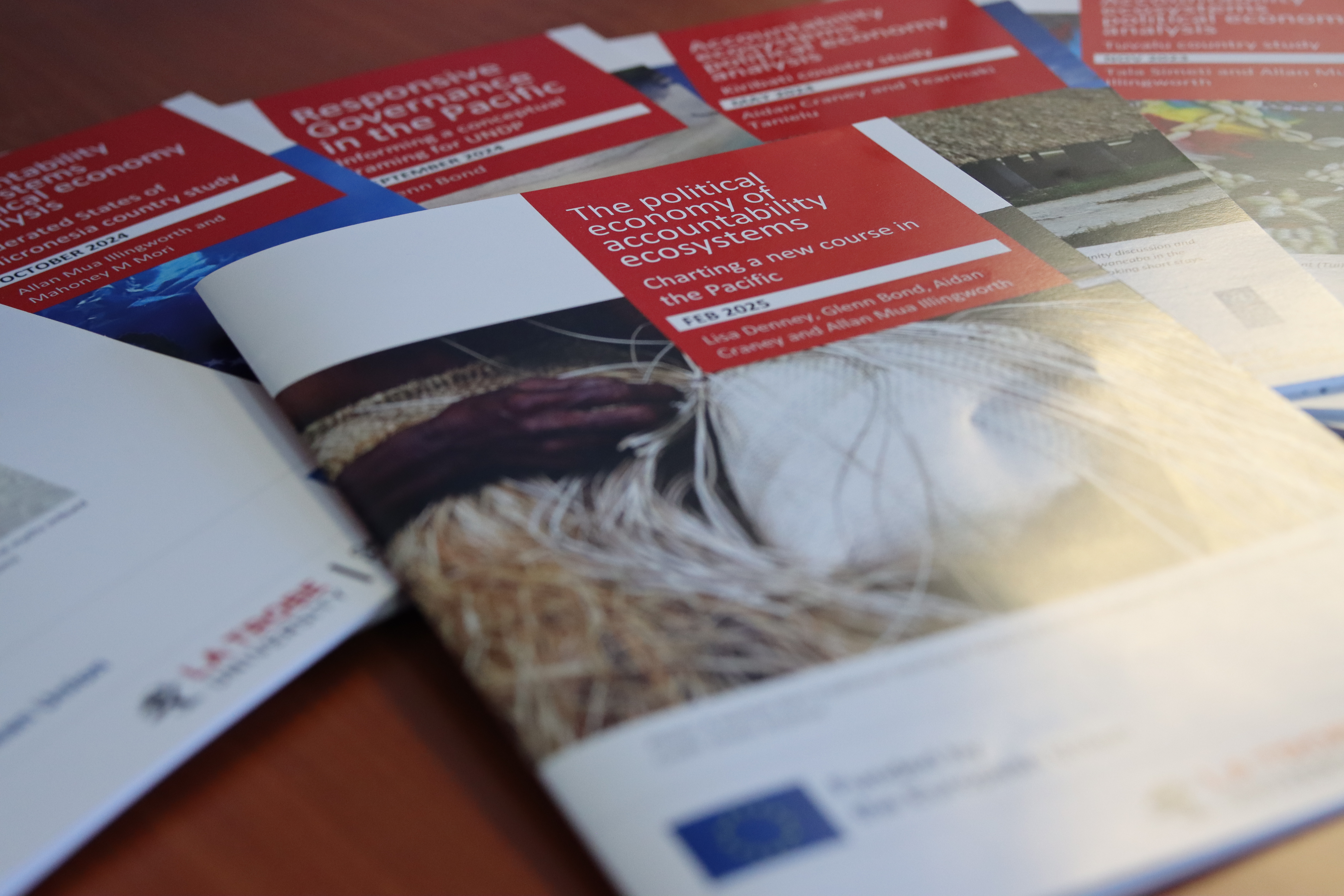Brochures with red and white covers stacked on a wooden table.
