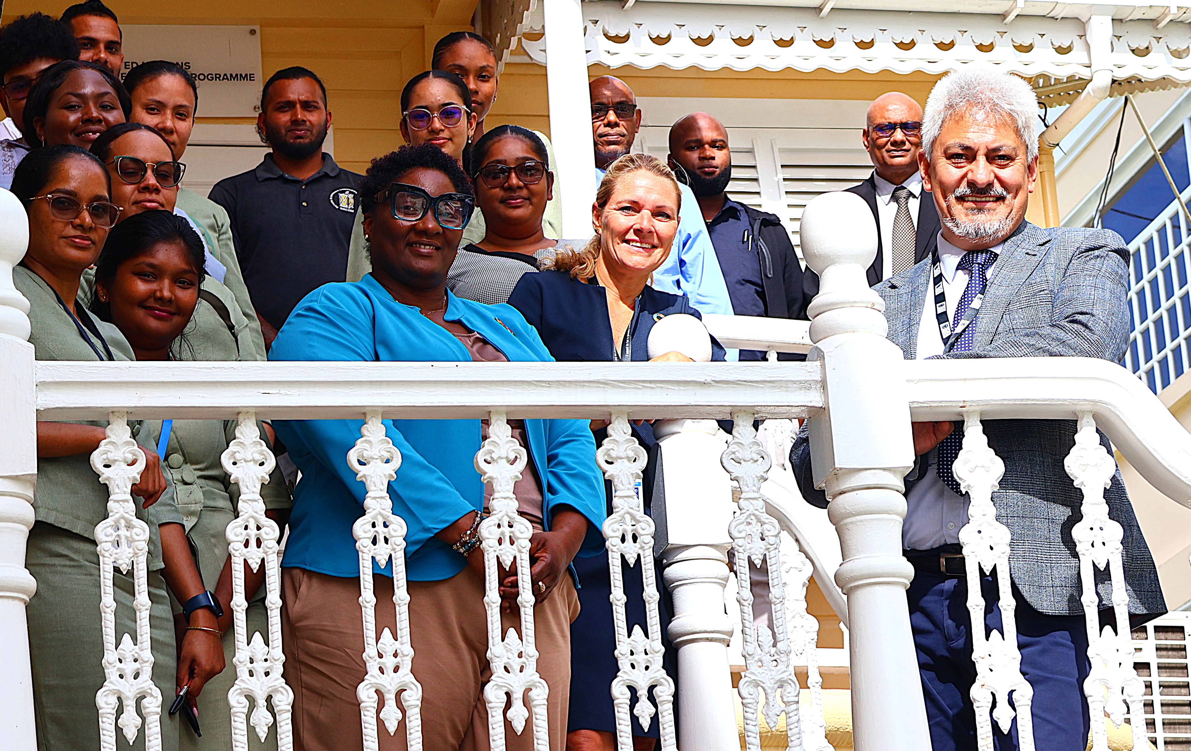 A group of diverse individuals poses on a balcony, smiling at the camera.