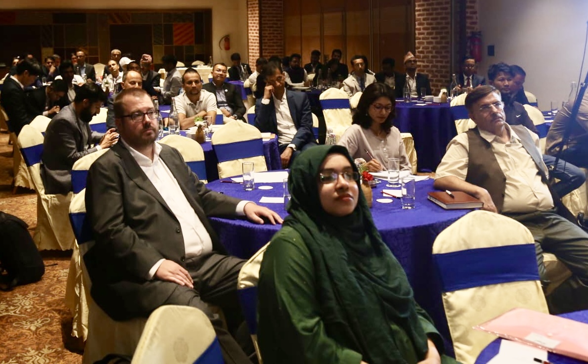 A diverse audience seated at tables, attentively listening in a seminar setting.